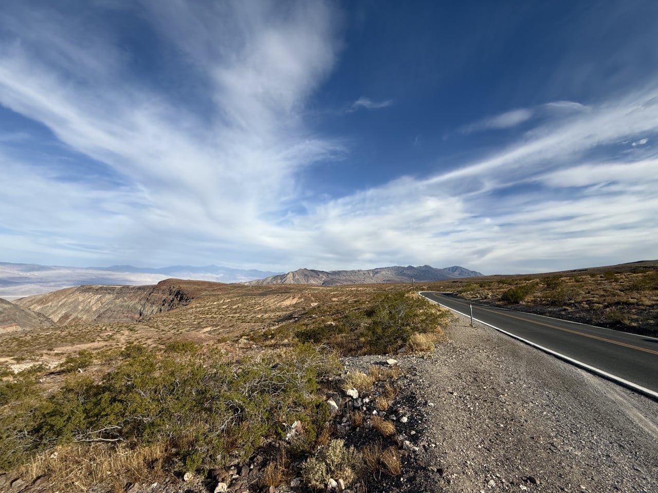 Pouštní silnice v Death Valley pod rozlehlou modrou oblohou s mraky