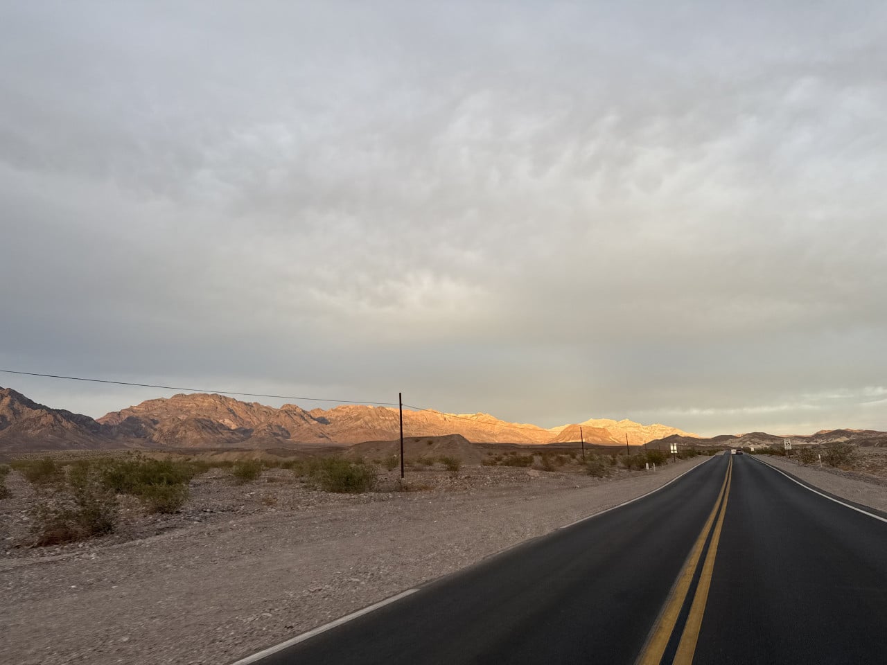 Silnice v Death Valley, poušť a osvětlené hory pod zataženou oblohou