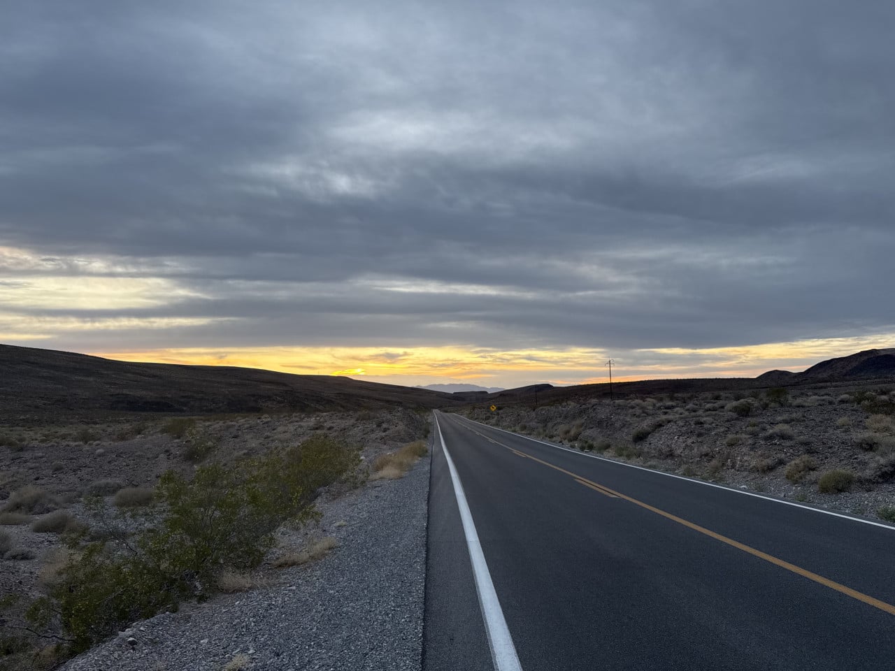 Pustá silnice v Death Valley při západu slunce, pod zamračenou oblohou.
