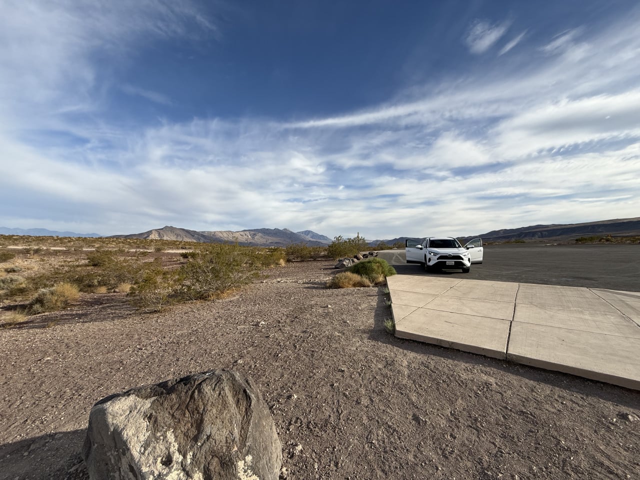 Auto s otevřenými dveřmi stojí na parkovišti v Death Valley pod rozlehlou oblohou
