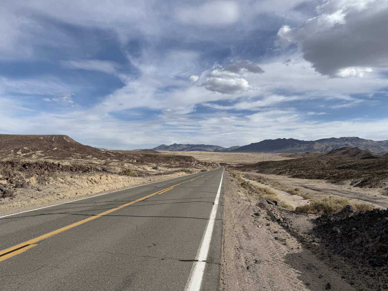 Silnice v Death Valley mezi holými horami pod dramatickou oblohou