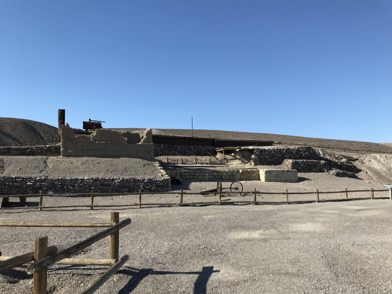 Písková krajina, zřícené kamenné stavby a dřevěné oplocení v Death Valley