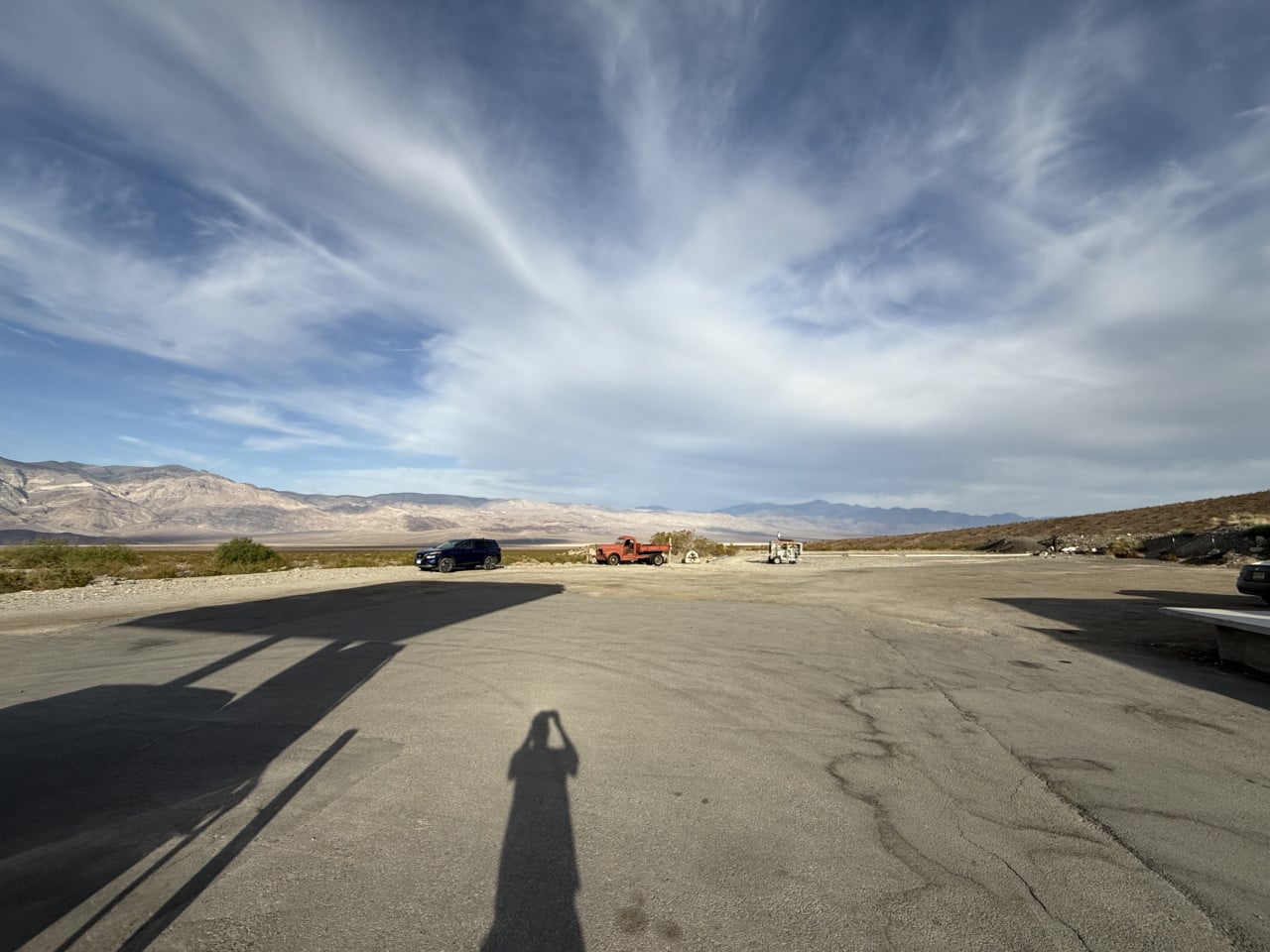 Parkoviště v Death Valley, auta, horské panorama a dlouhý stín fotografa.