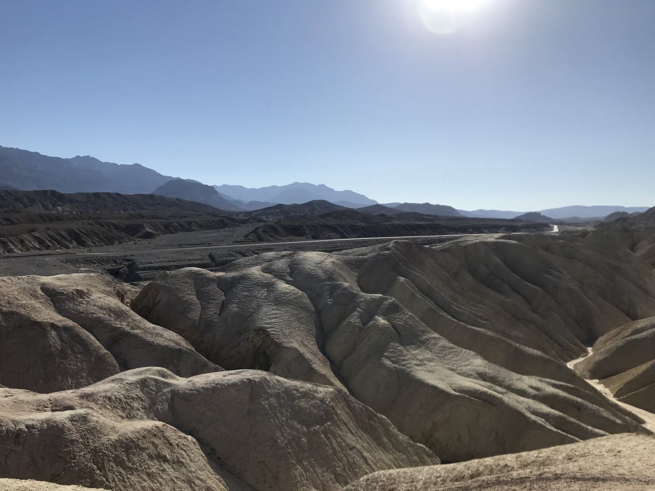 Kamenité údolí Death Valley s dunami, silnicí a jasným sluncem nad horami