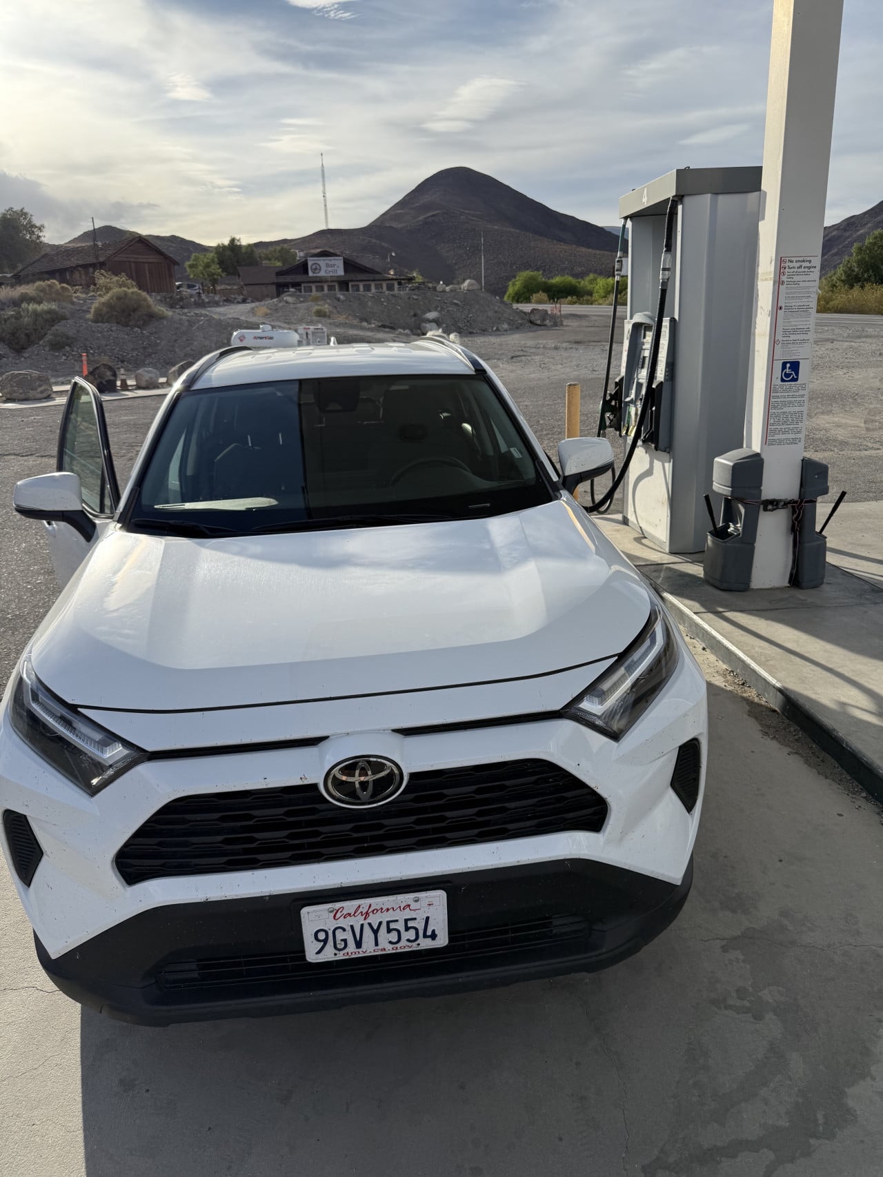 Bílá Toyota u čerpací stanice v pouštní krajině Death Valley, horám v pozadí.