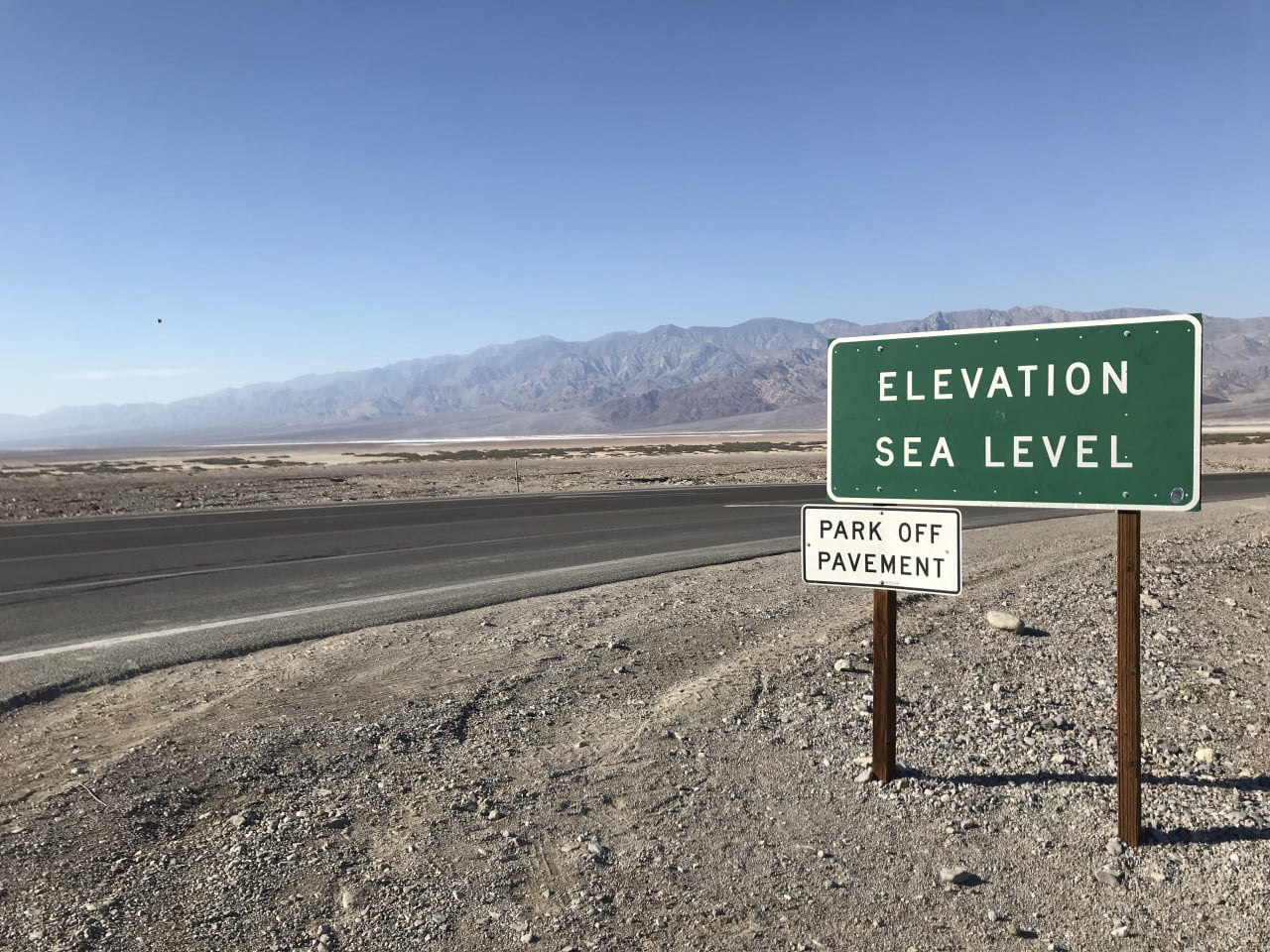 Cedule v Death Valley u nejnižšího bodu mořské hladiny, silnice a hory v pozadí