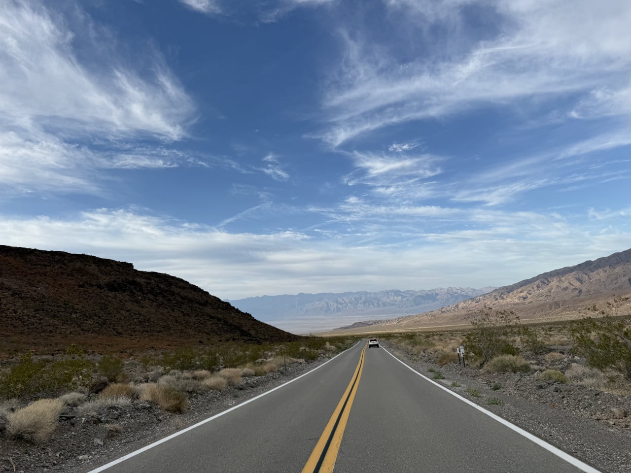 Silnice v Death Valley mezi horami, pod modrou oblohou a bílými mraky