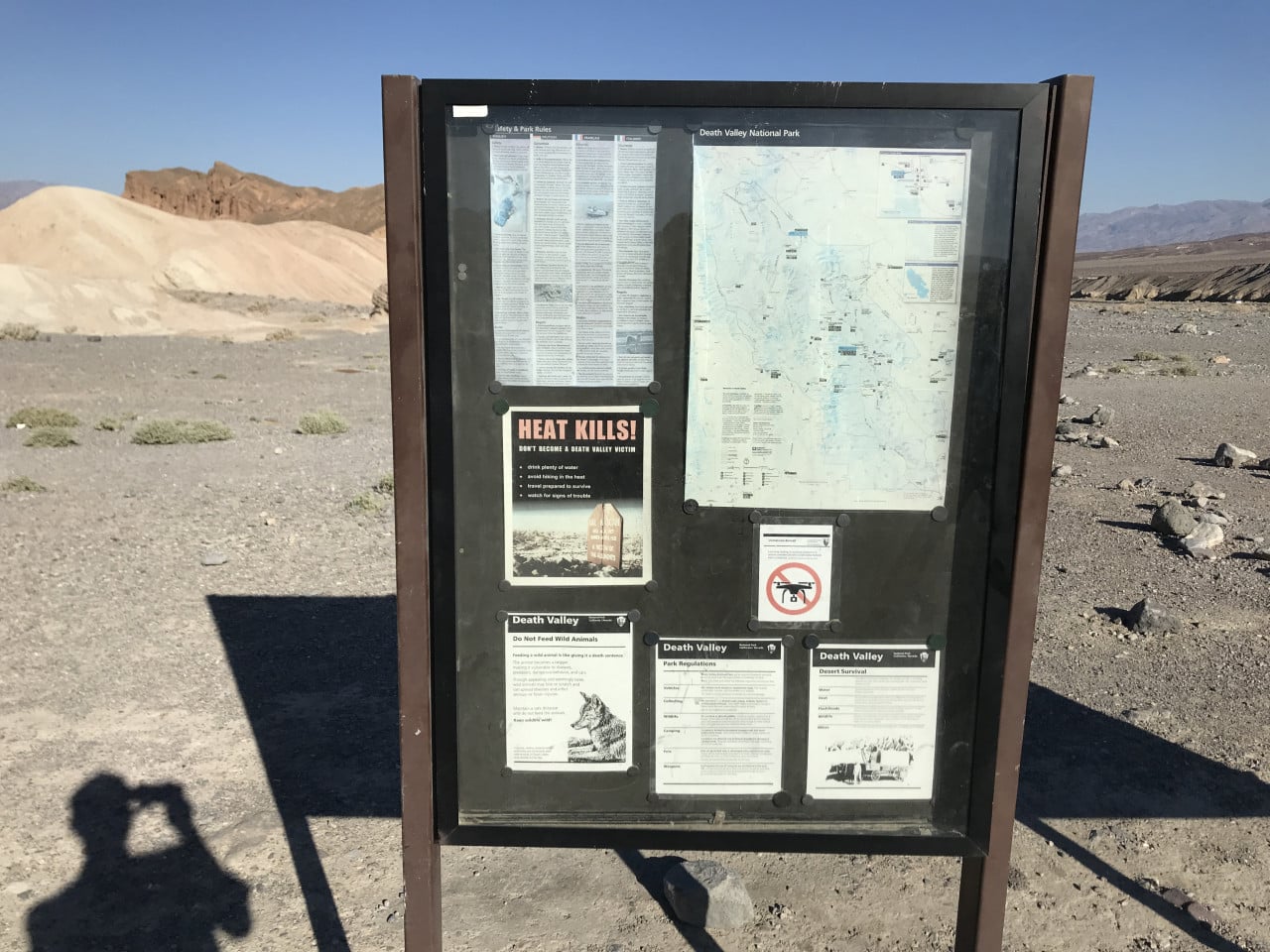Informační tabule Death Valley National Park v pouštní krajině se stínem fotografa.