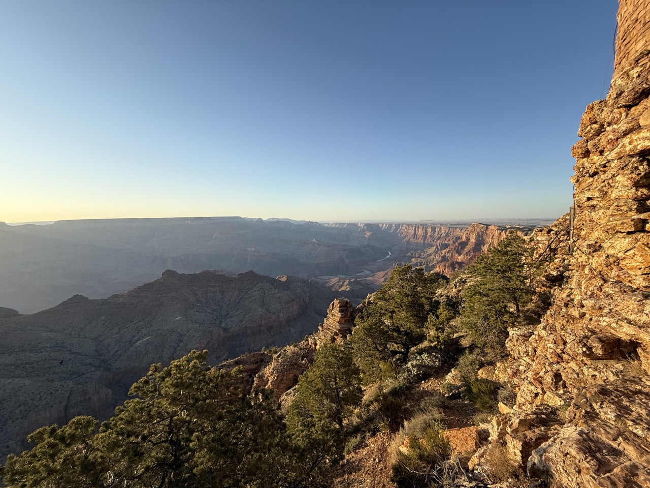 Západ slunce nad Grand Canyonem s skalní stěnou a borovicemi