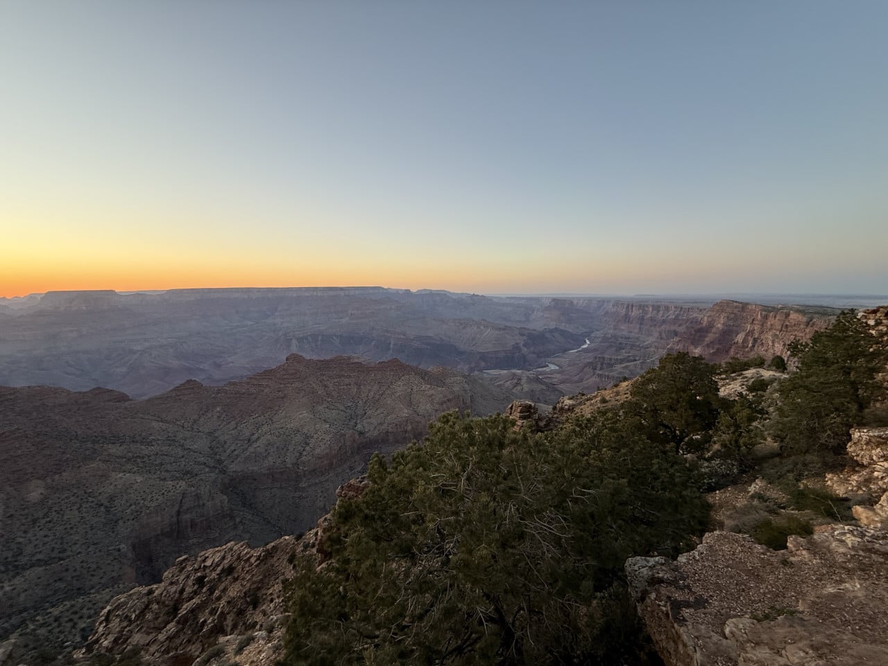Západ slunce nad Grand Canyonem z vyhlídky Desert View, skalnaté okraje a řeka Colorado níže