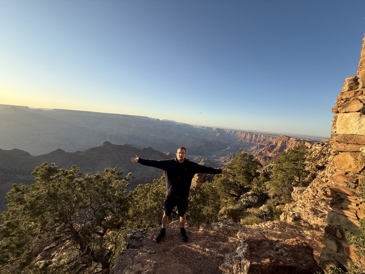 Muž s rozpaženýma rukama na vyhlídce Grand Canyonu při západu slunce