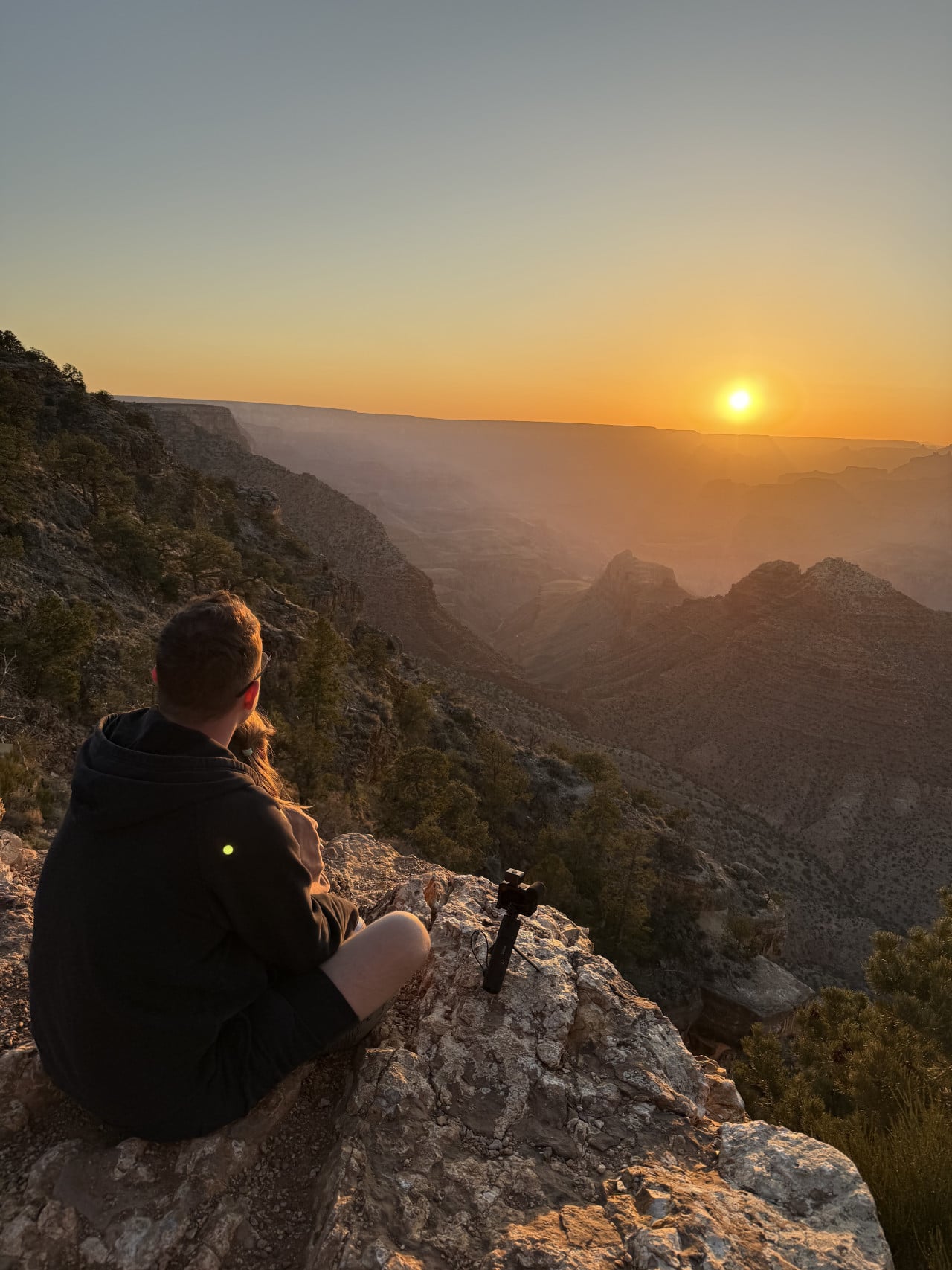 Muž s dítětem sleduje západ slunce nad Grand Canyonem z útesu.