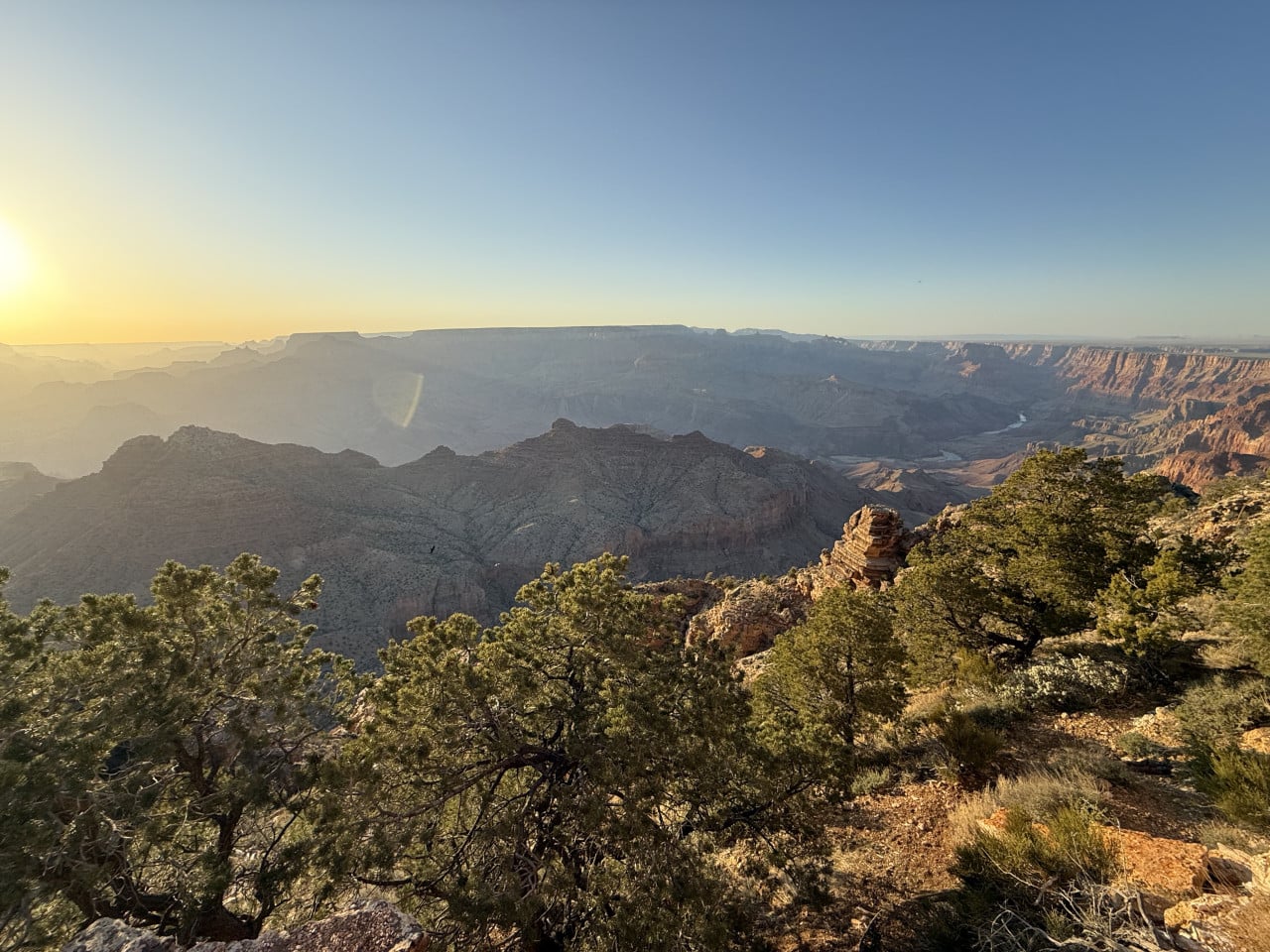Západ slunce nad Grand Canyonem s borovicemi v popředí‬