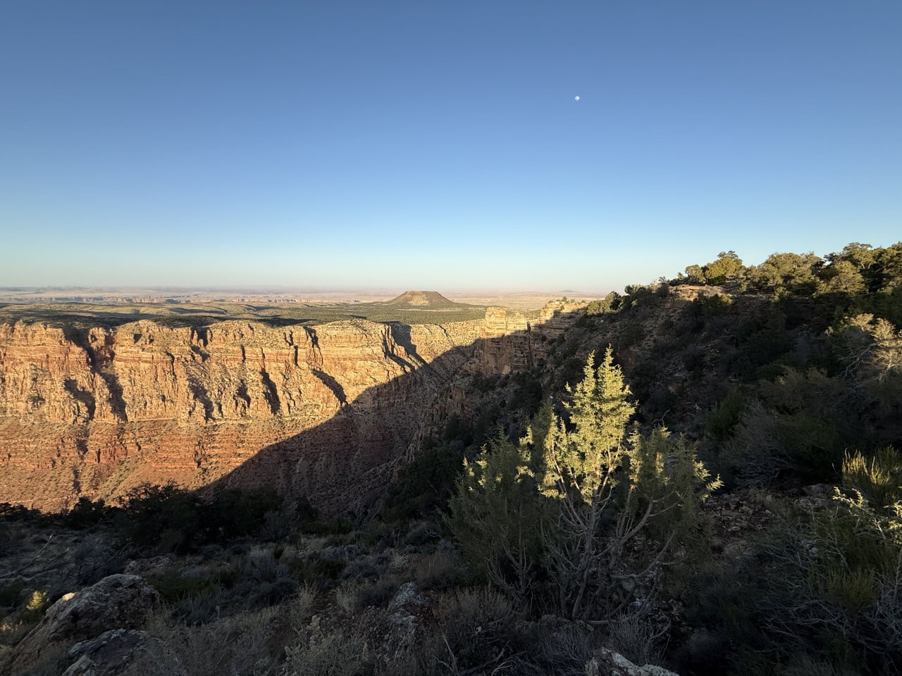 Výhled na Grand Canyon při západu slunce, skalní stěny a modrá obloha s měsícem