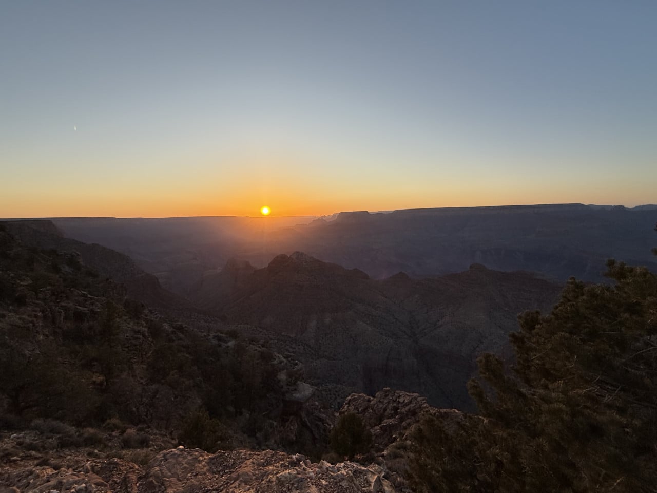 Západ slunce nad Grand Canyonem z Desert View Point, skalnaté okraje v popředí