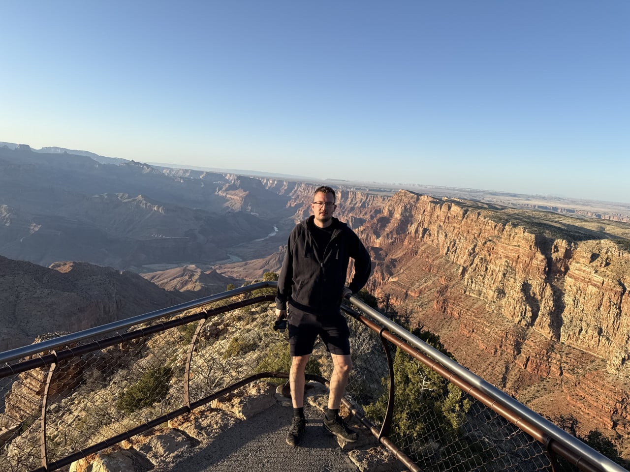 Muž stojí na vyhlídce Desert View nad Grand Canyonem při západu slunce.