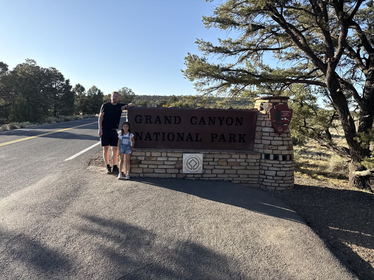 Muž a dívka u kamenné cedule GRAND CANYON NATIONAL PARK u silnice