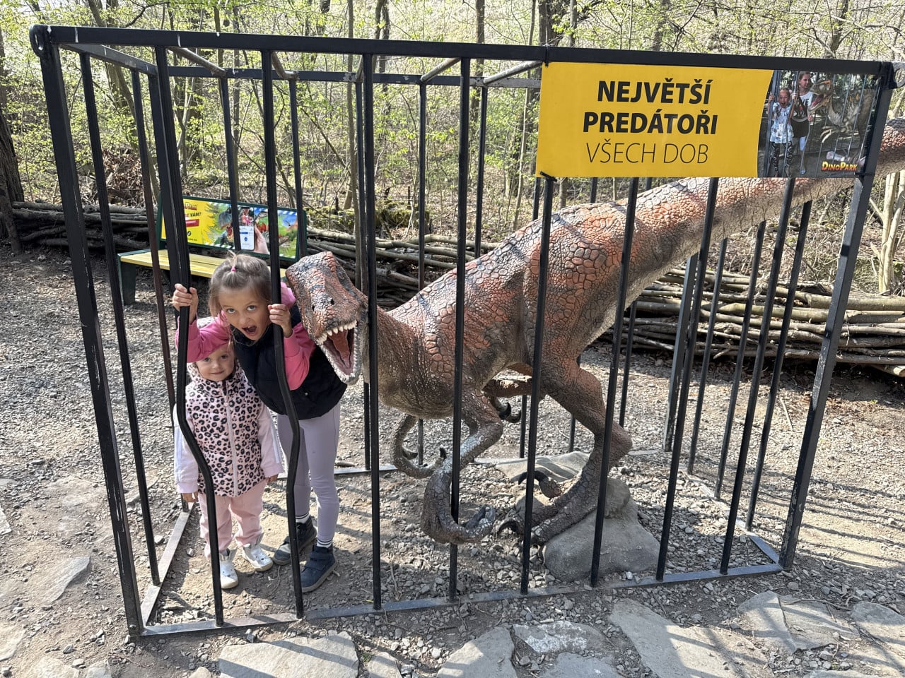 Děti u klece s dinosaurem, cedule Největší predátoři všech dob.