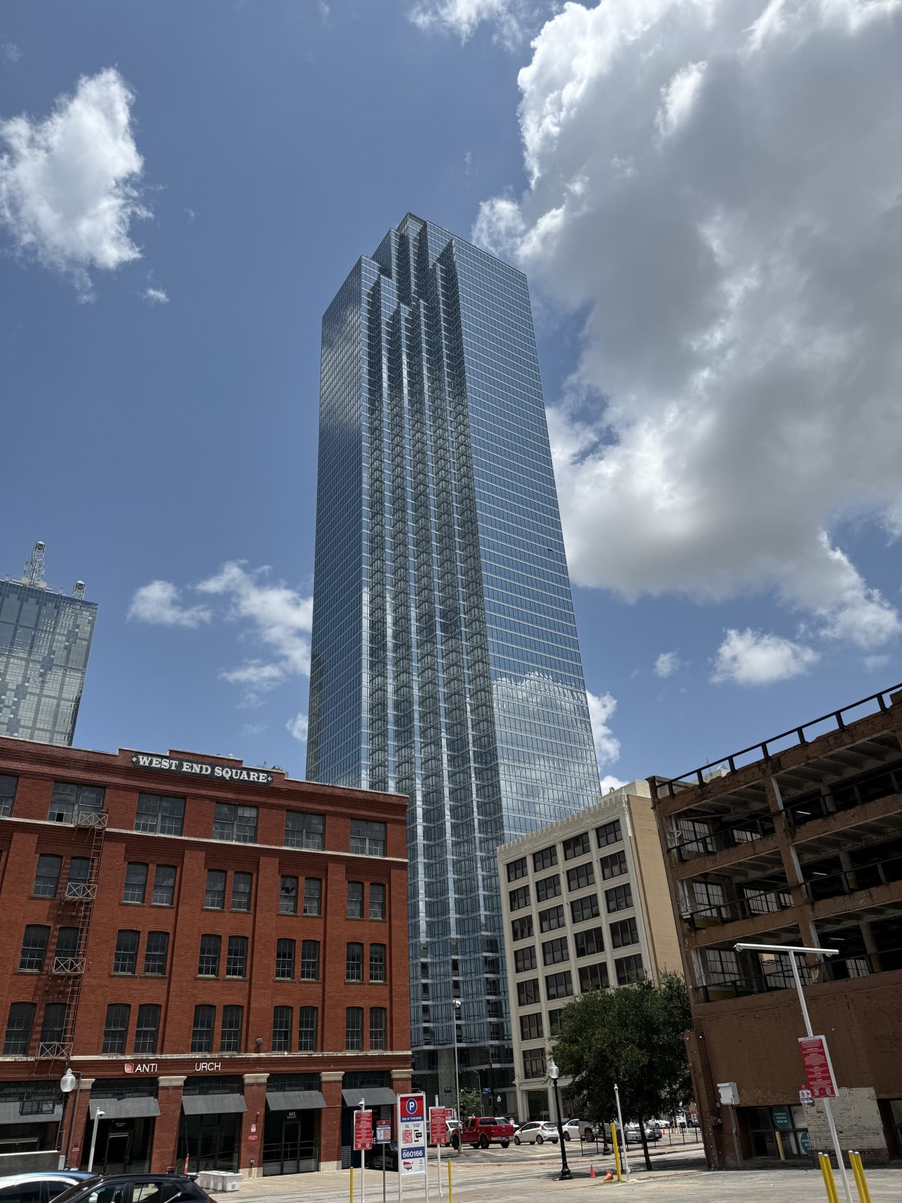 Skleněný mrakodrap nad cihlovými domy, nápis WEST END SQUARE, modrá obloha