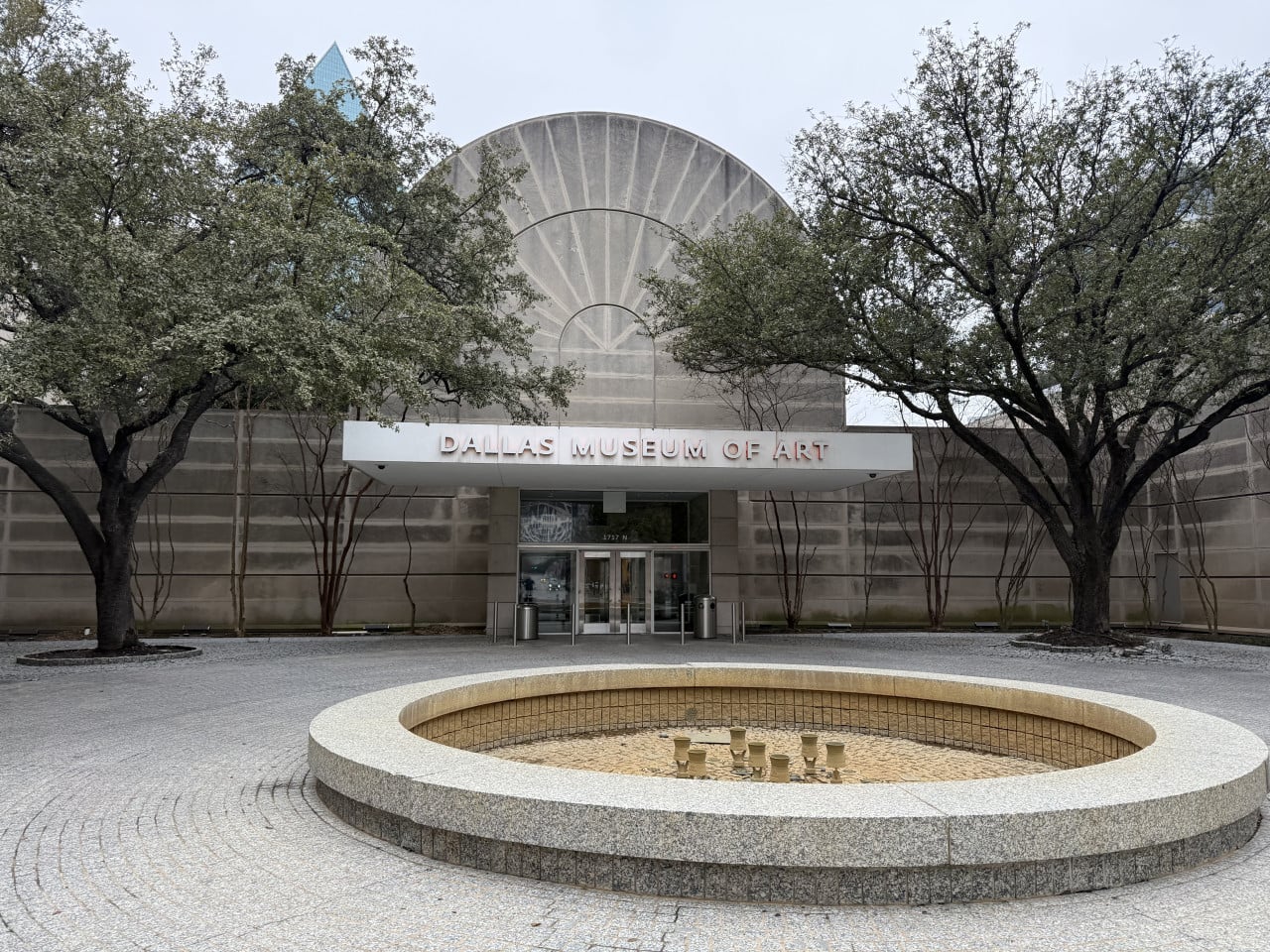 Vchod do DALLAS MUSEUM OF ART, stromy a prázdná kruhová fontána před budovou.