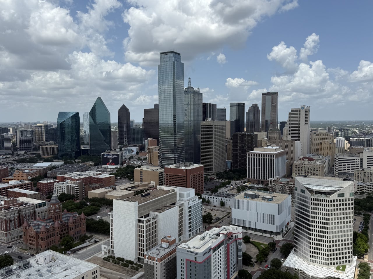 Panorama downtown Dallas s mrakodrapy, budovami Westin a Courtyard pod oblačnou oblohou.