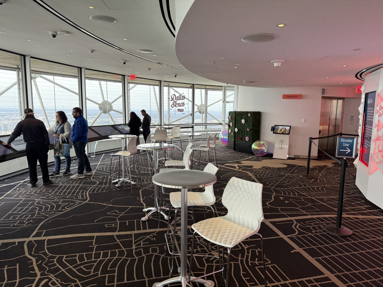 Vyhlídková místnost s okny, stoly, lidmi; nápisy Dallas Texas, PHOTO KIOSK, Elevator Line.