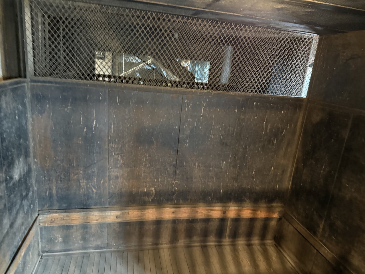 Interiér staré kovové kabiny s pletivem nahoře a dřevěným madlem