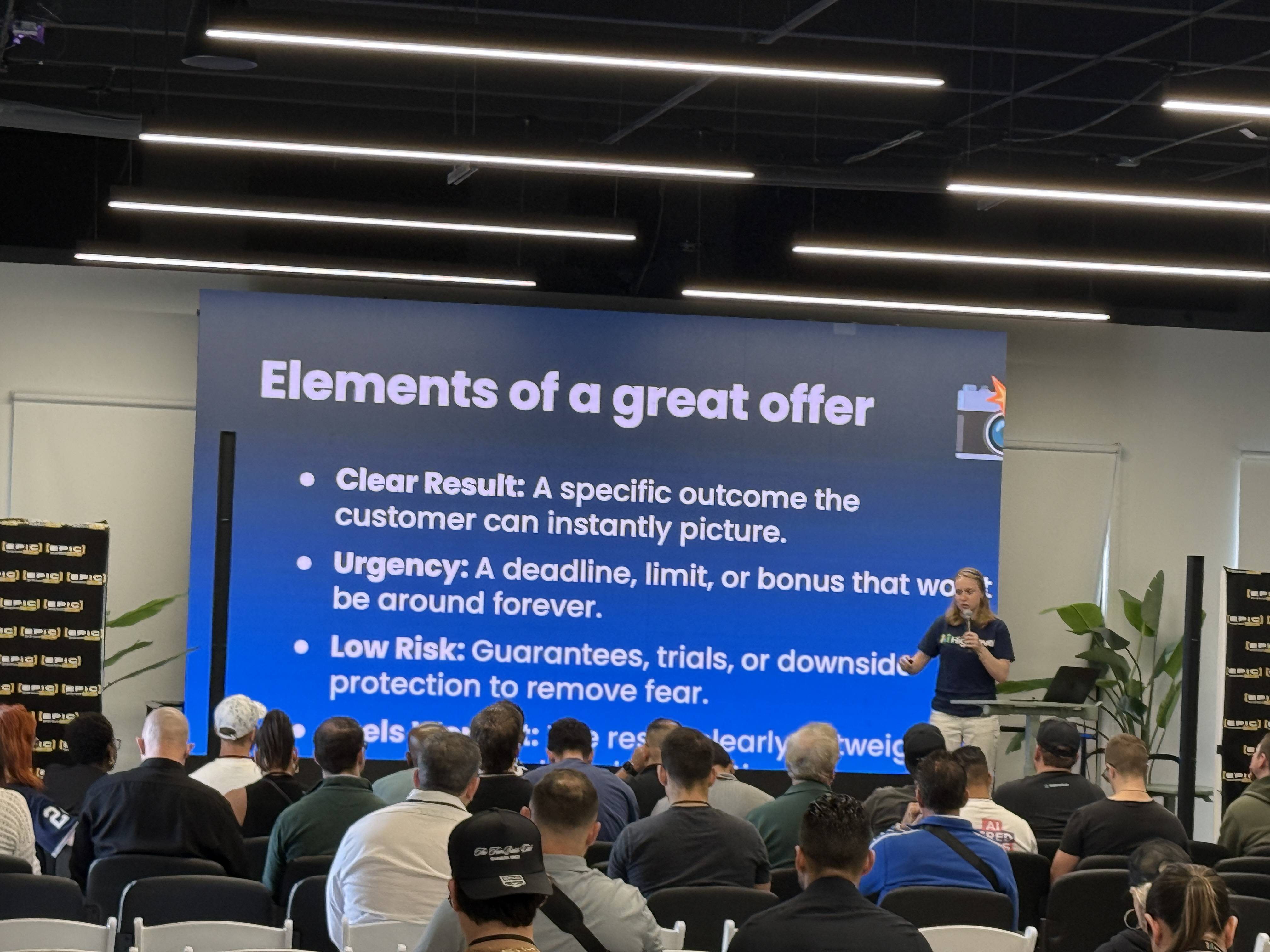Přednášející před publikem, slide Elements of a great offer: Clear Result, Urgency, Low Risk.
