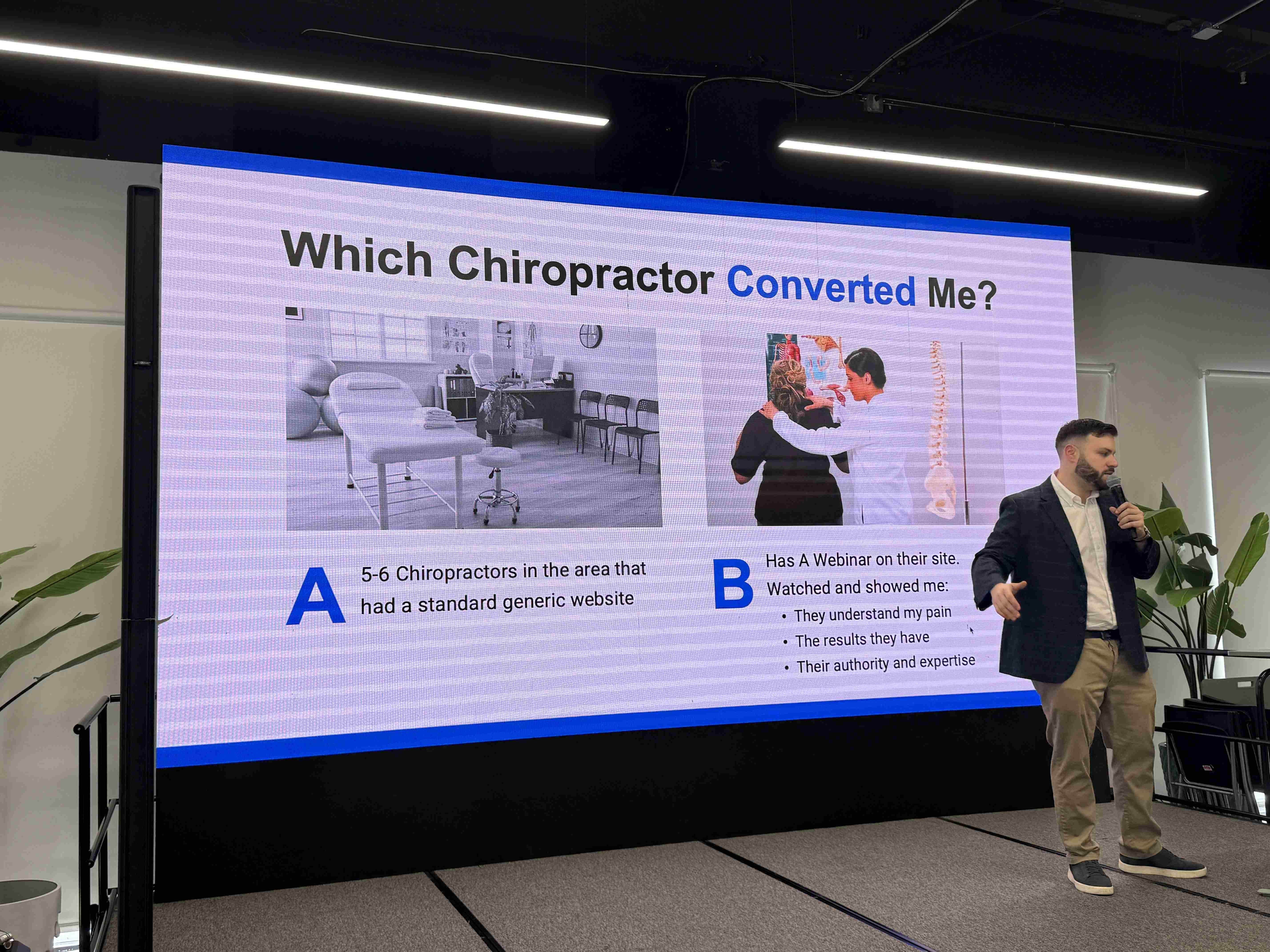 Přednášející s mikrofonem u projekce Which Chiropractor Converted Me? na konferenčním pódiu