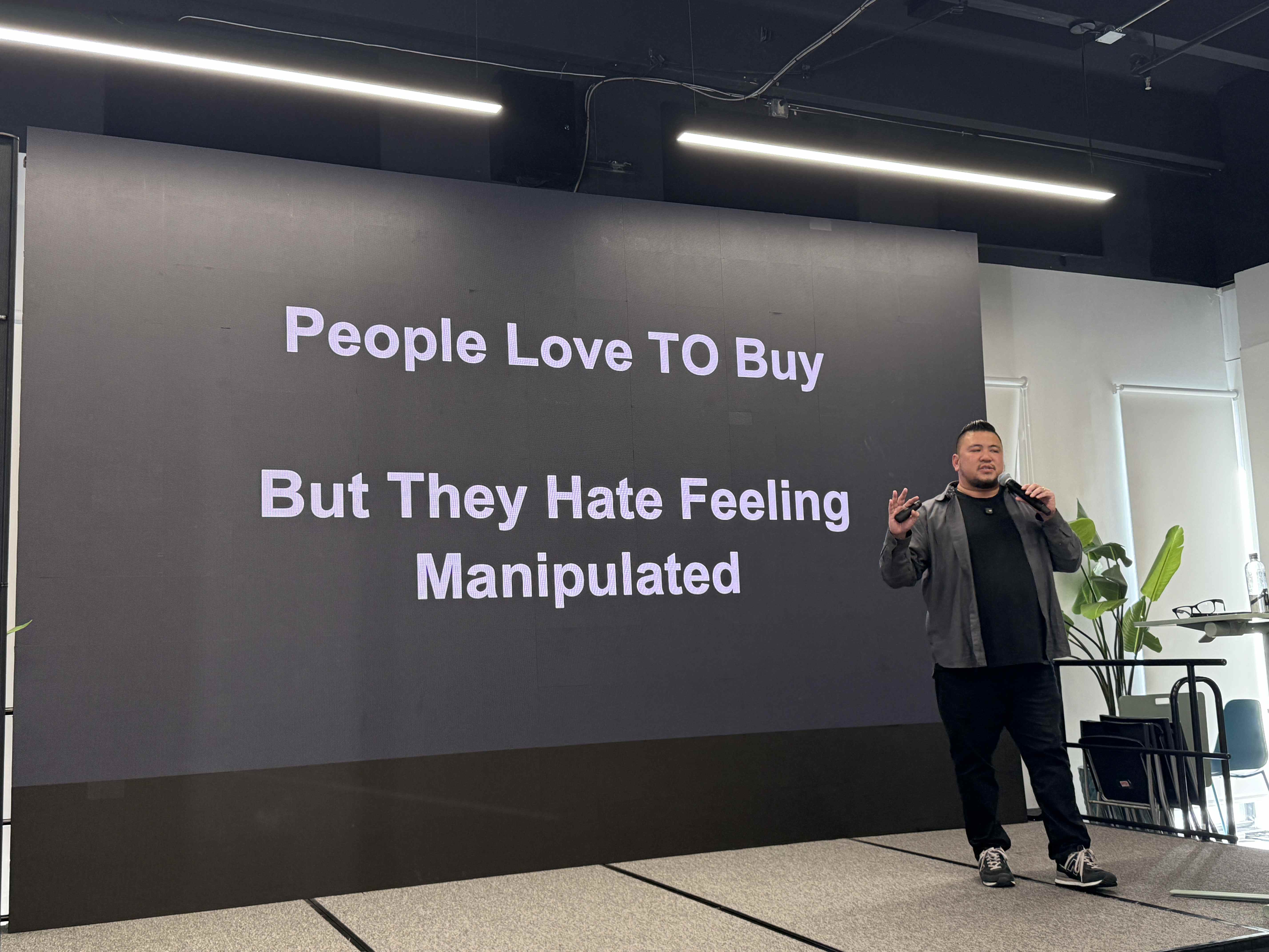 Slide: People Love TO Buy But They Hate Feeling Manipulated; řečník na pódiu.