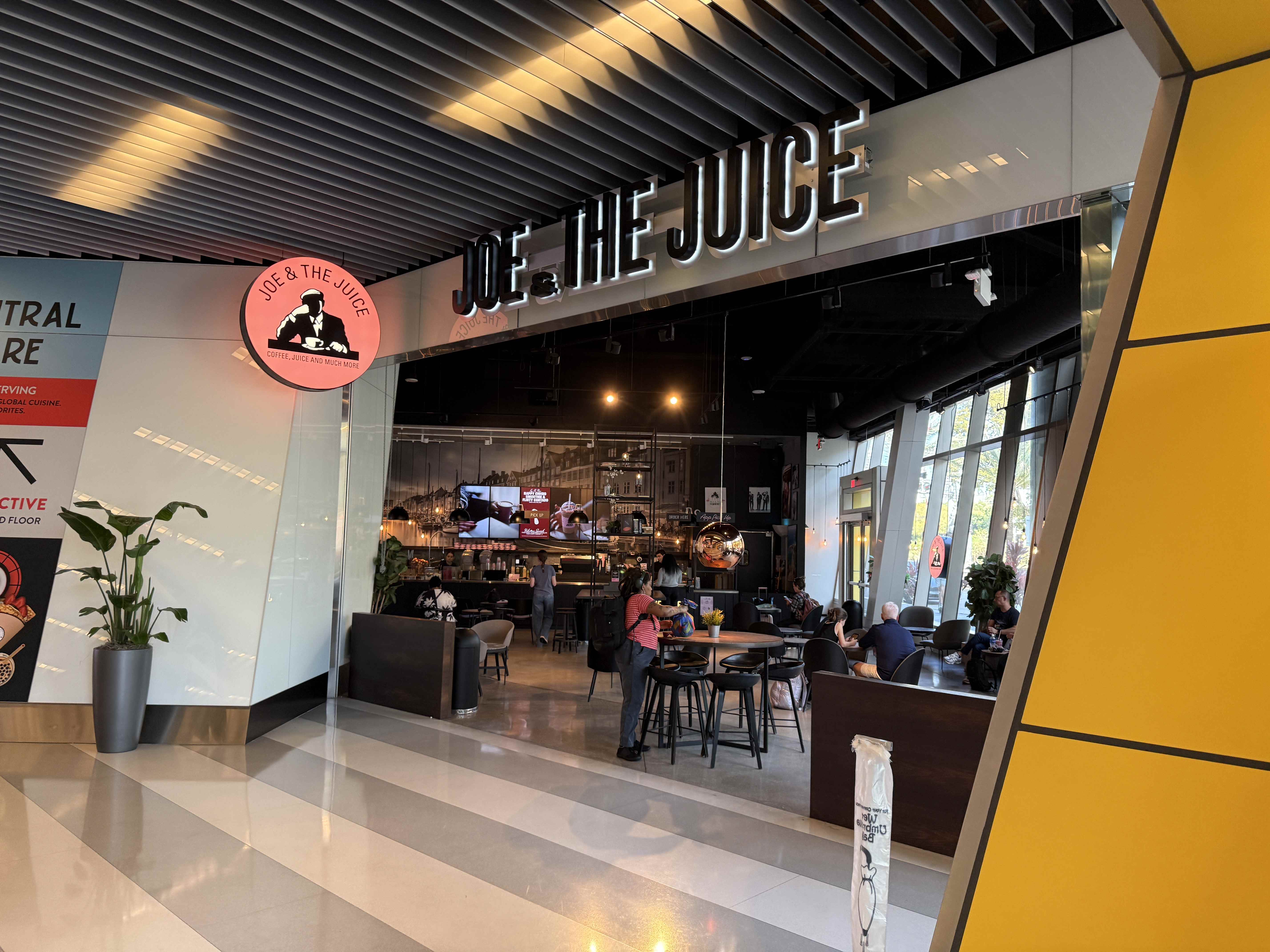 Vstup do kavárny JOE & THE JUICE, uvnitř sedí hosté u stolů.
