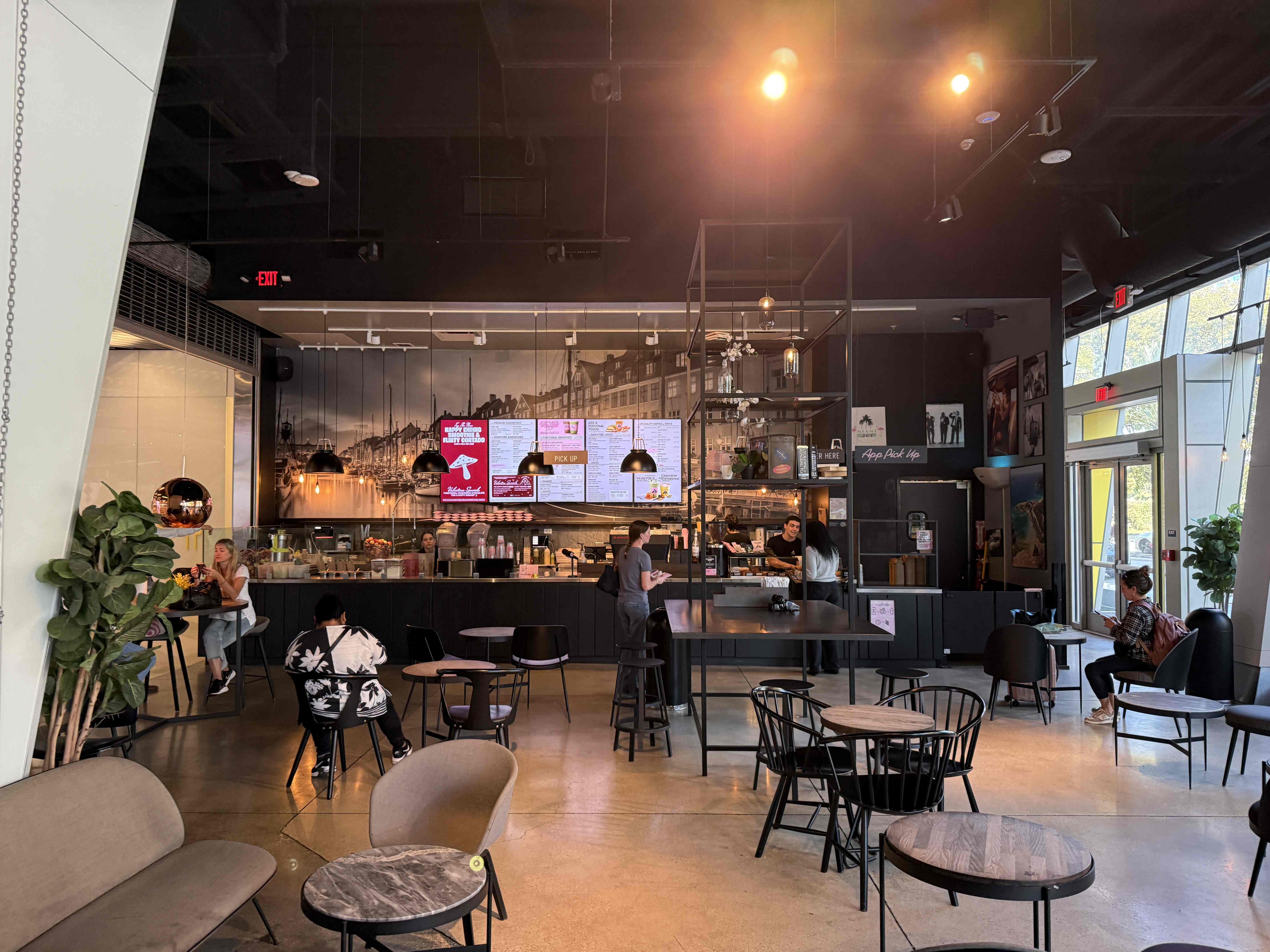 Interiér kavárny s barem, obrazovkami menu a nápisy EXIT, PICK UP, App Pick Up.