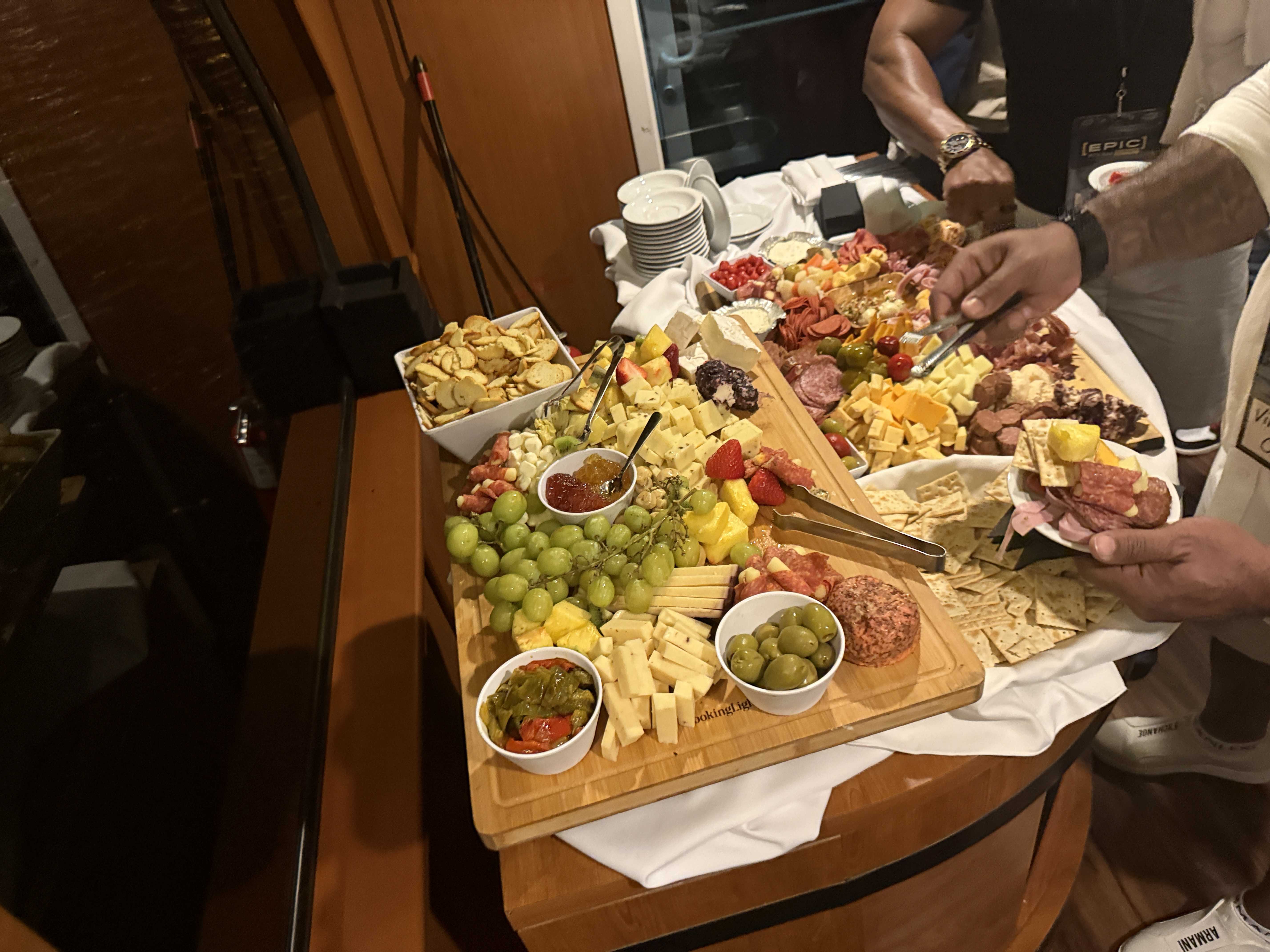 Ruce účastníků u rautu: sýry, uzeniny, ovoce, krekry, visačka EPIC