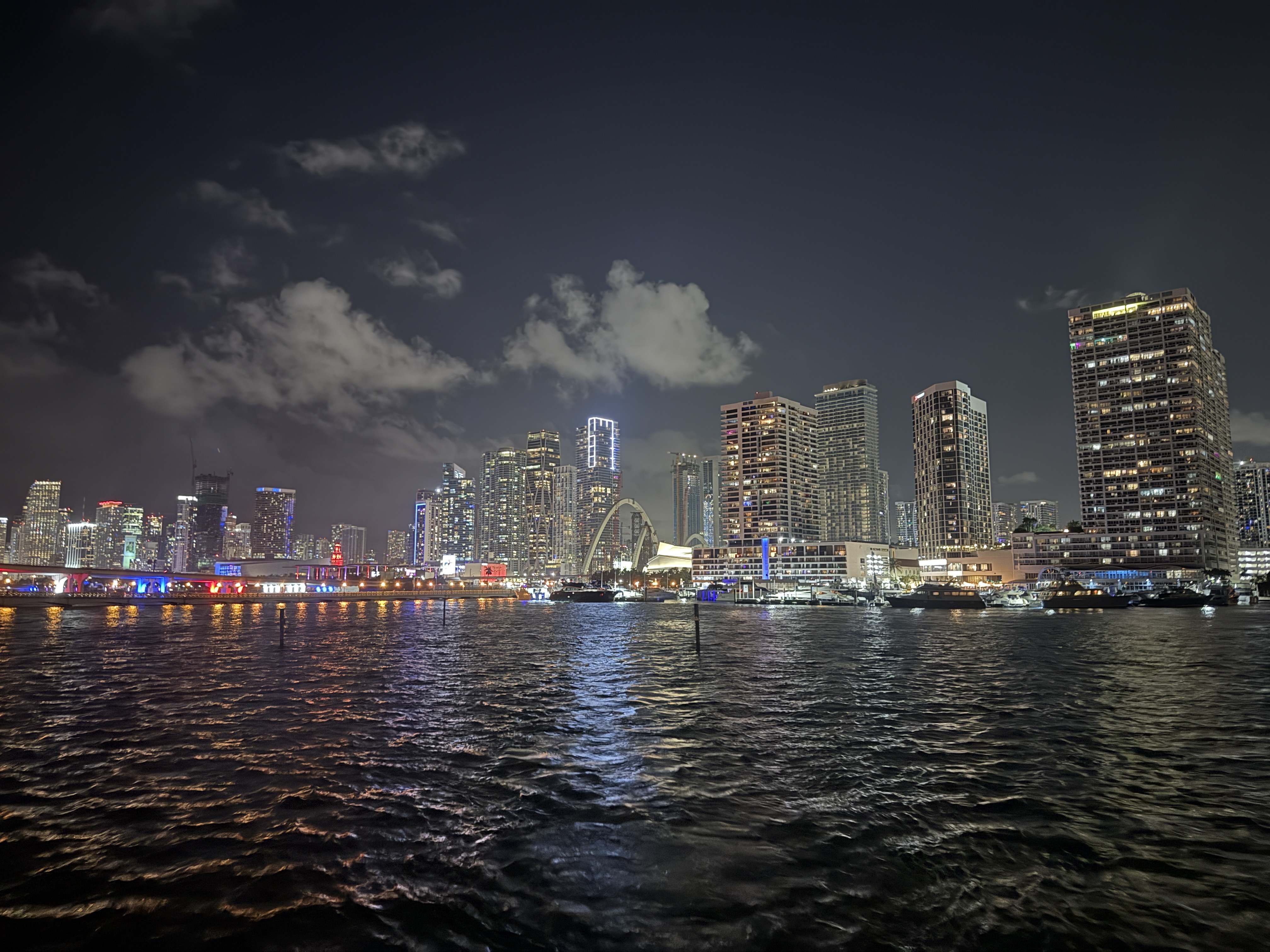 Noční panorama Miami, osvětlené mrakodrapy a most, odraz světel na vodě