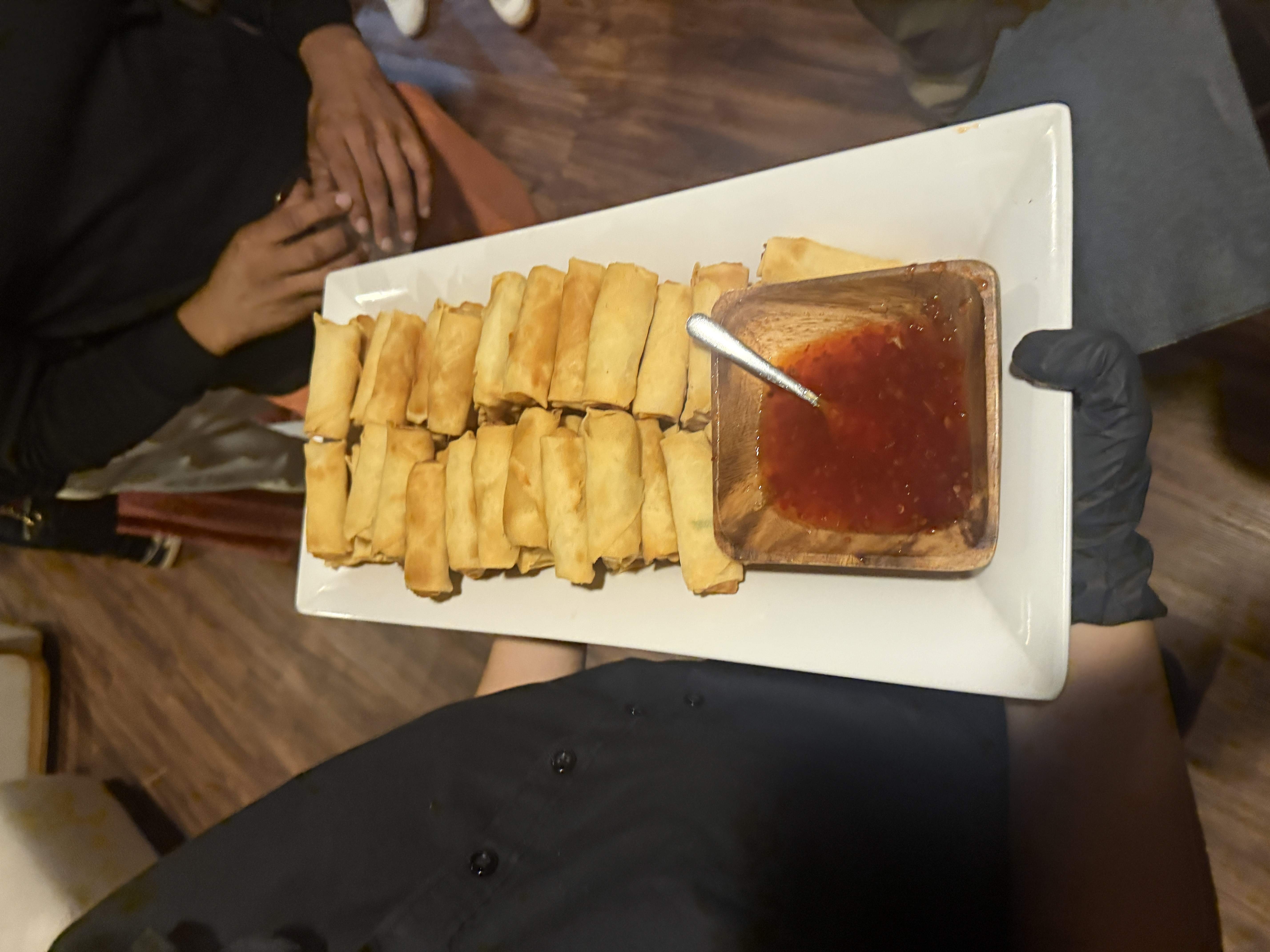 Číšník v rukavicích nese talíř jarních závitků s chilli omáčkou