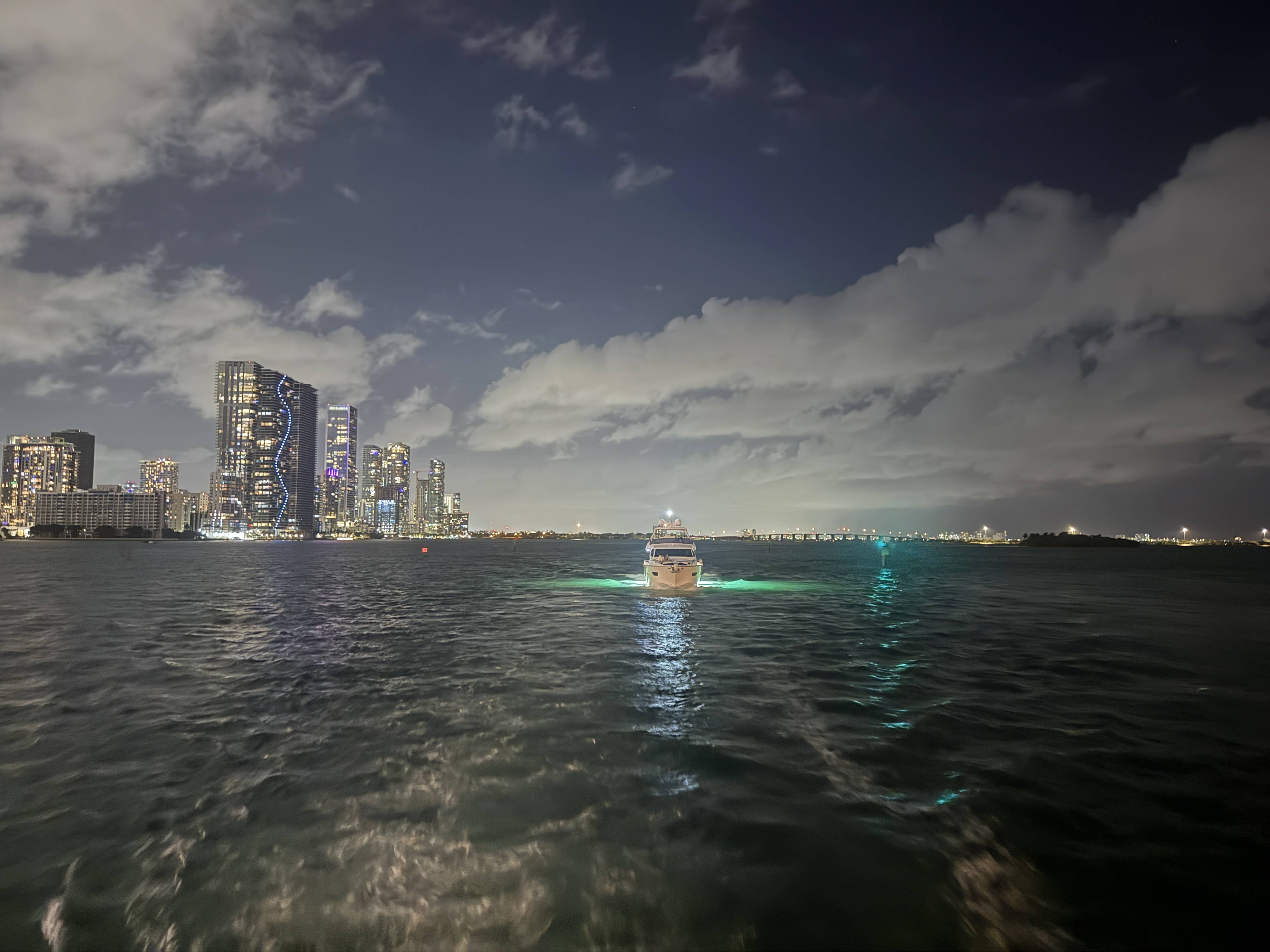 Noční panorama Miami, osvětlené mrakodrapy vlevo a loď se zeleným světlem