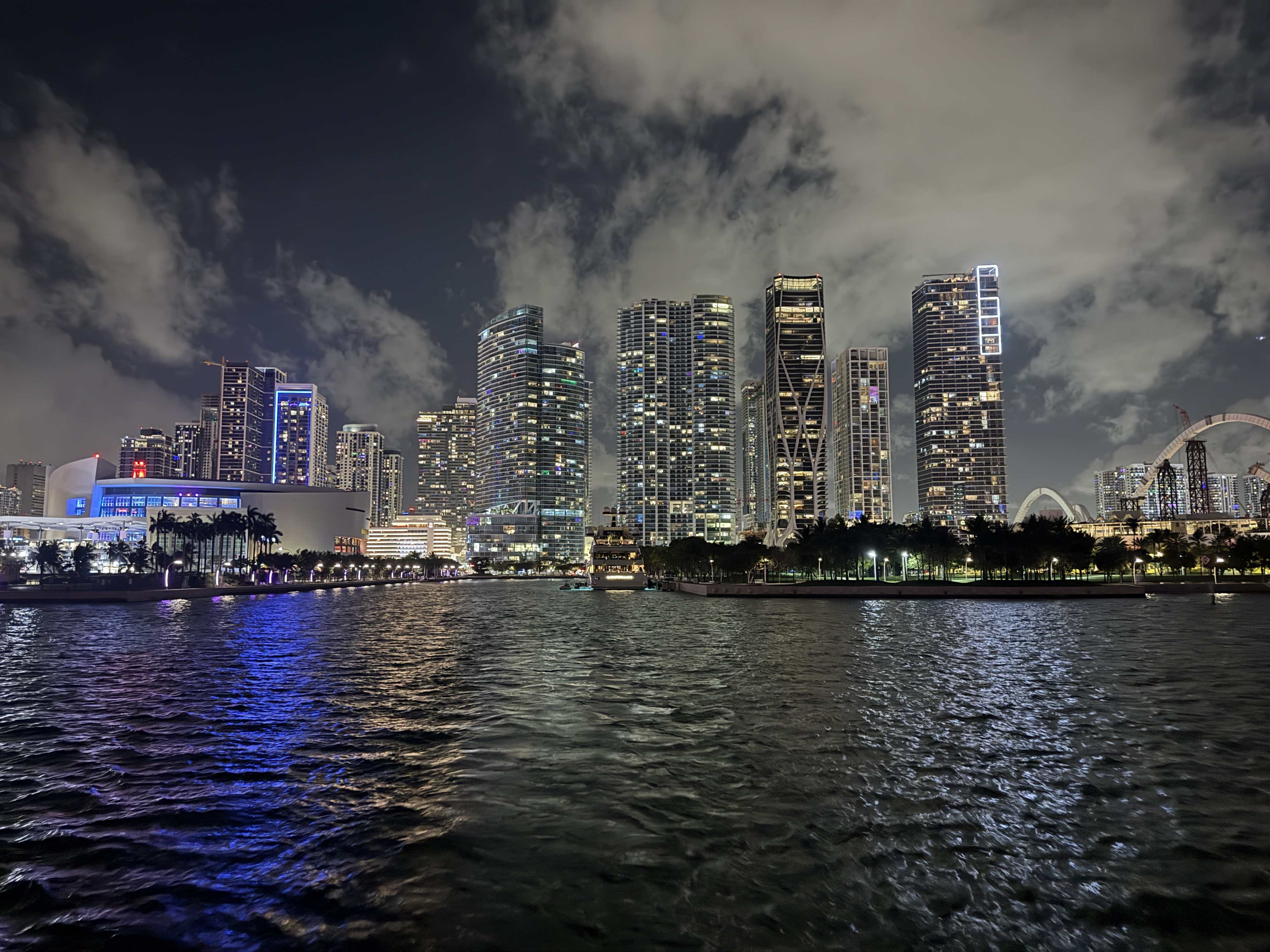 Noční panorama Miami: osvětlené mrakodrapy, oblaka, vodní hladina s odlesky