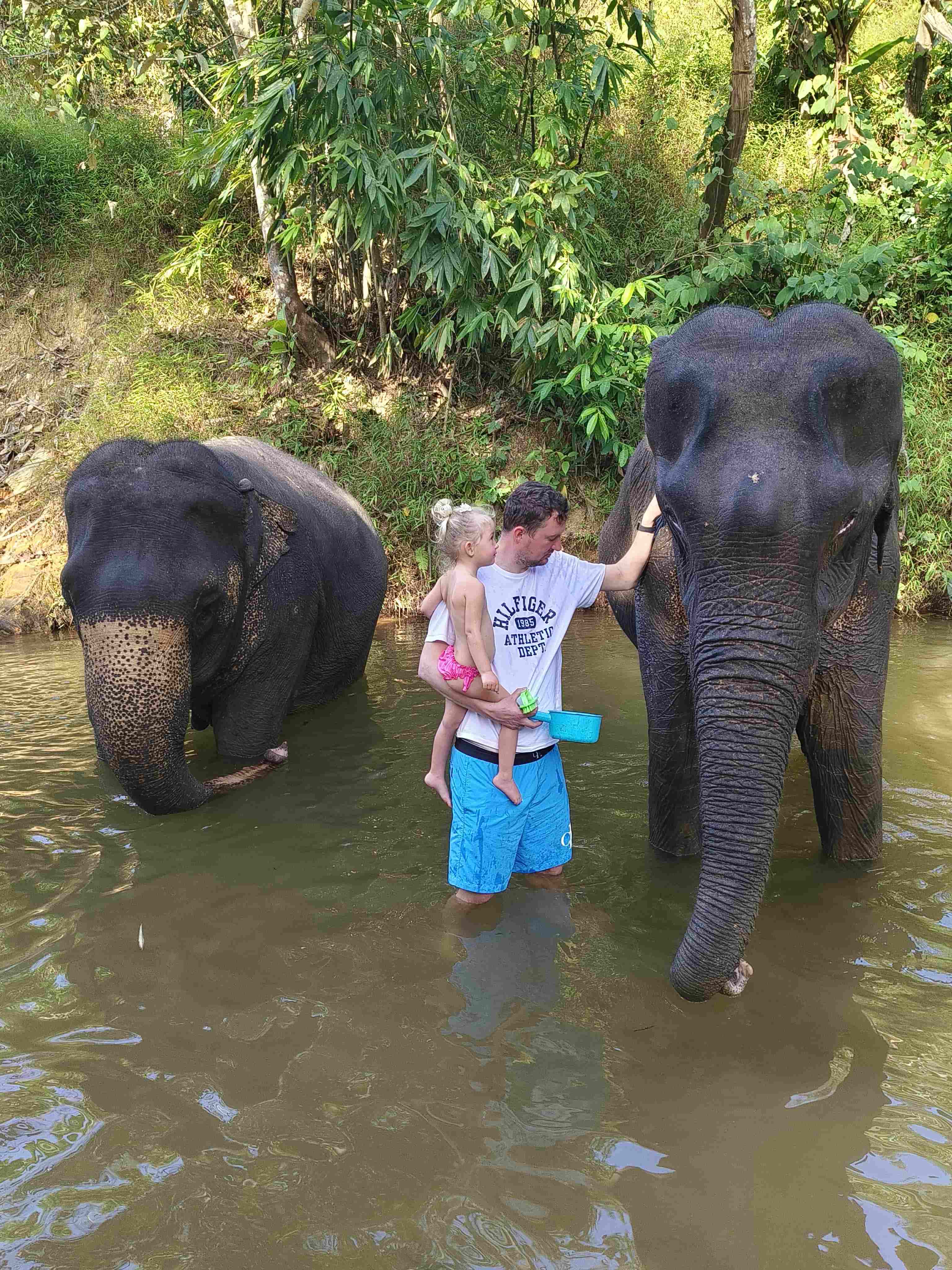 Muž s dítětem v řece hladí slona; tričko HILFIGER ATHLETIC DEPT.