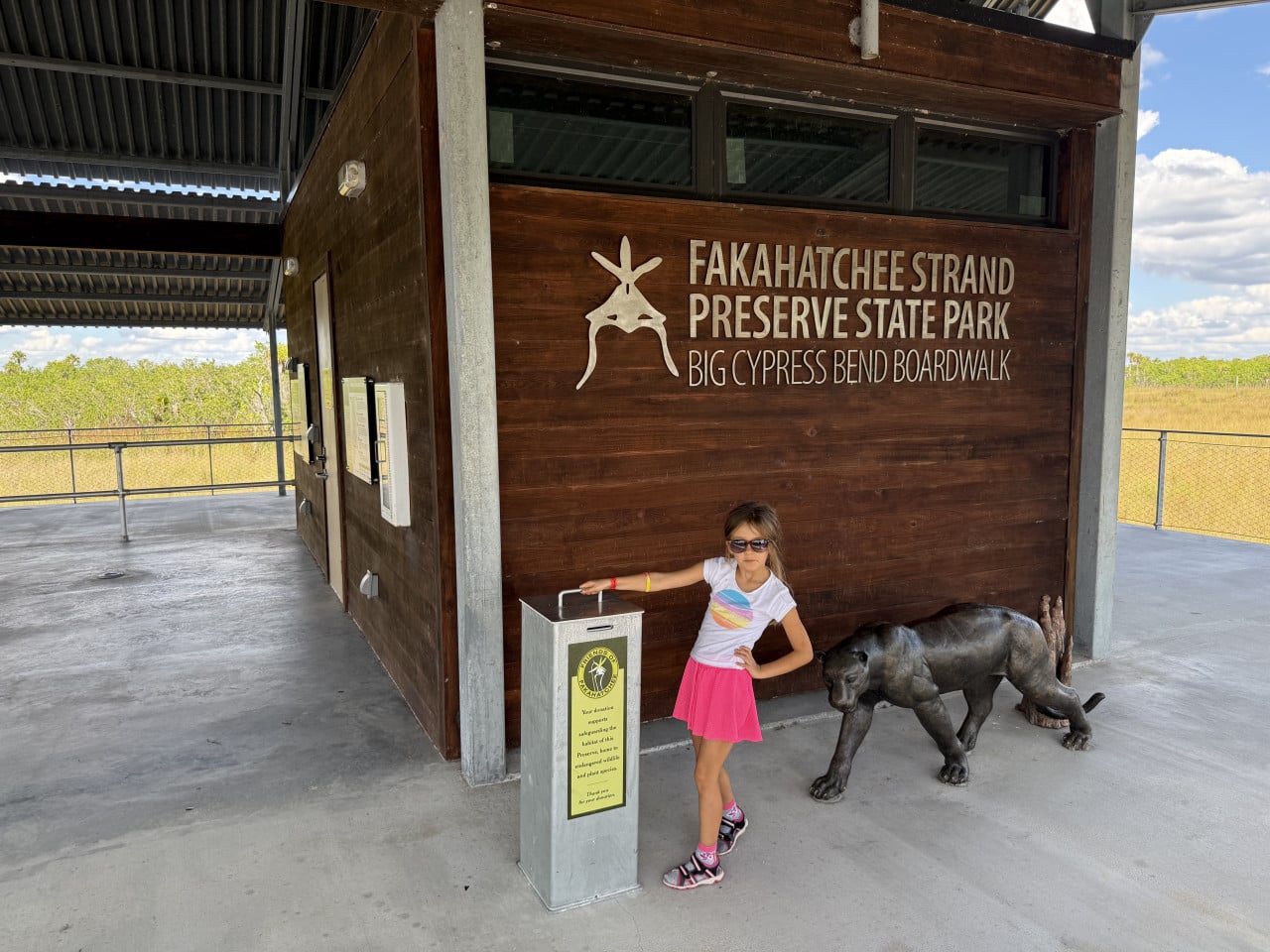 Dívka u budovy s nápisem Fakahatchee Strand Preserve State Park a sochou pantera.