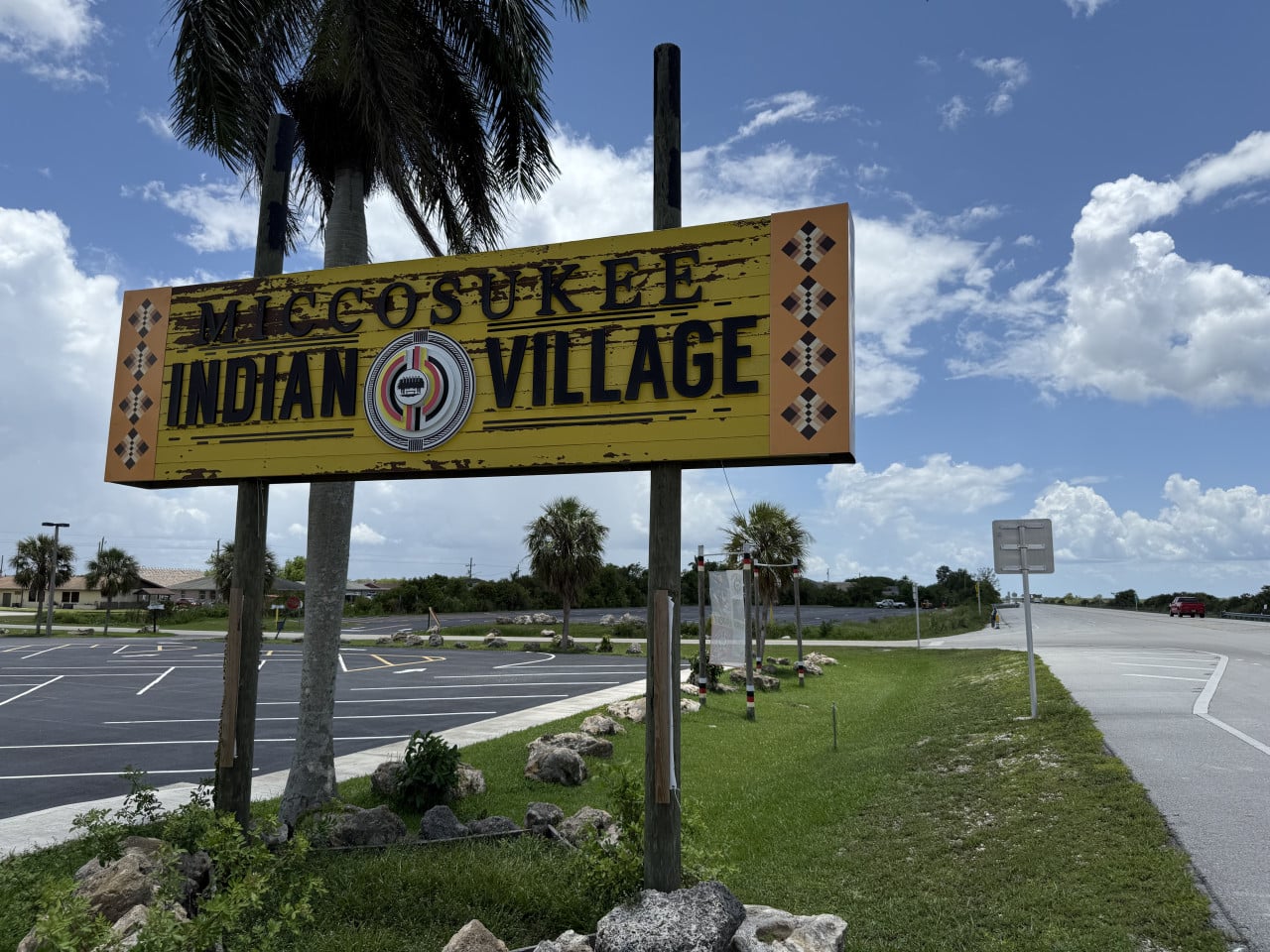 Cedule Miccosukee Indian Village u silnice pod palmami a modrou oblohou