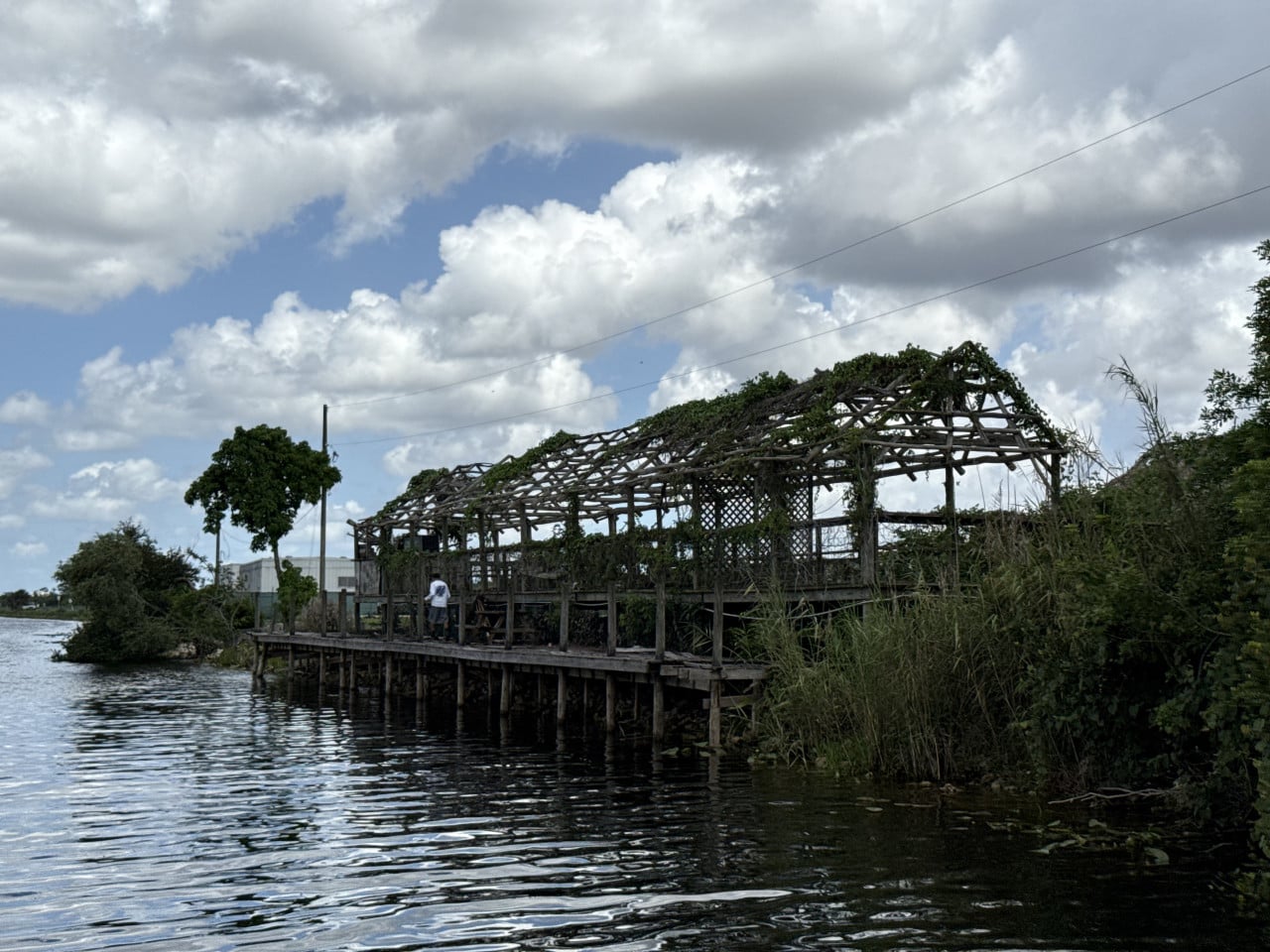 Dřevěná indiánská chýše na molu nad vodou v Everglades, pod oblohou s mraky.