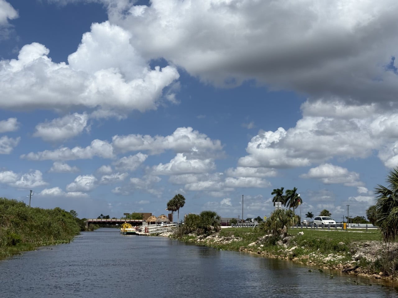 Kanál v Everglades, mola s airboatem, palmy a parkoviště pod oblačnou oblohou