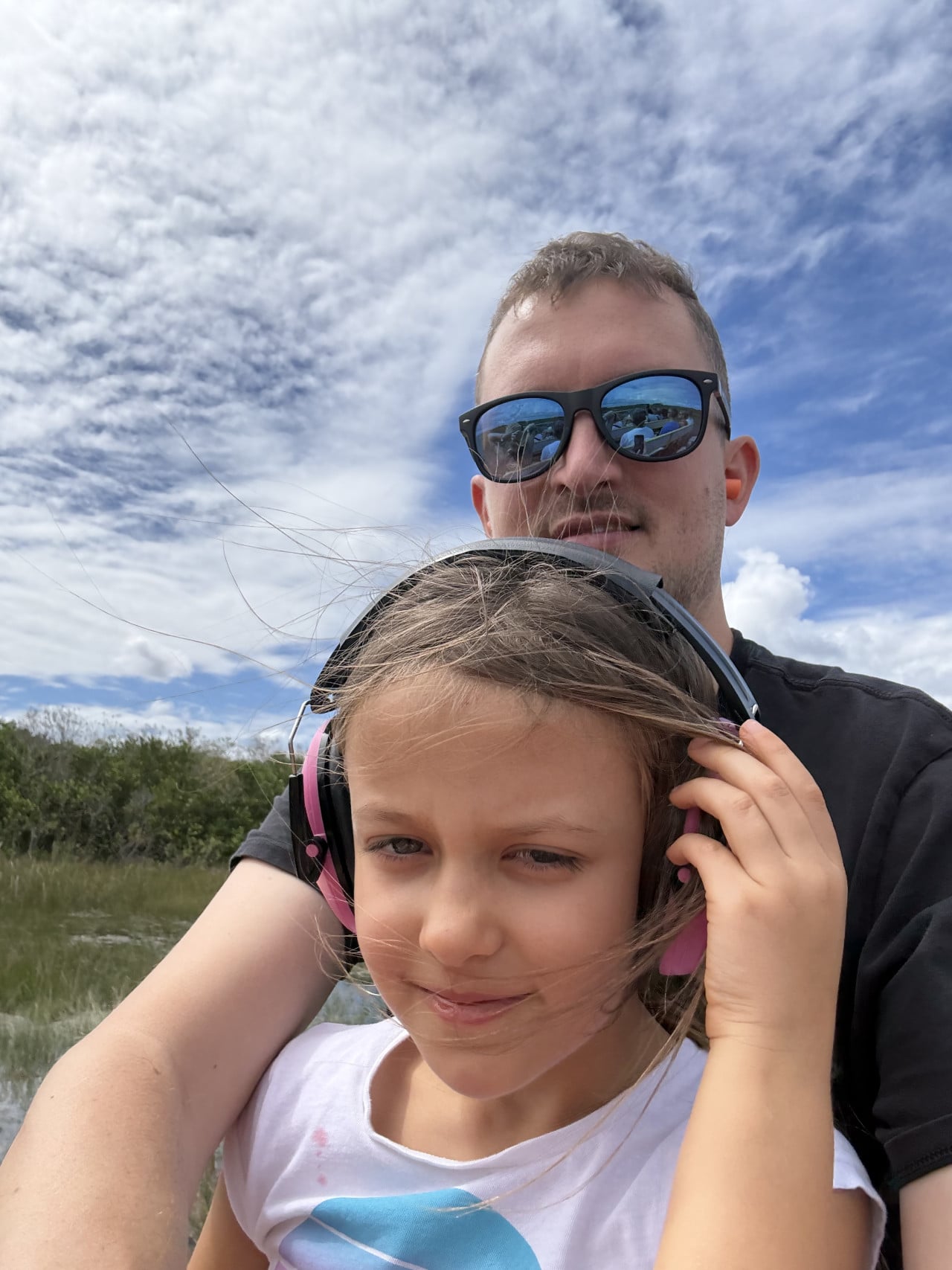 Muž a dívka na airboatu v Everglades, oba s ochrannými sluchátky.