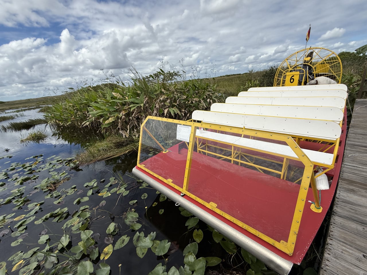 Airboat s bílými sedadly u mokřadu v Everglades, pod zataženou oblohou.