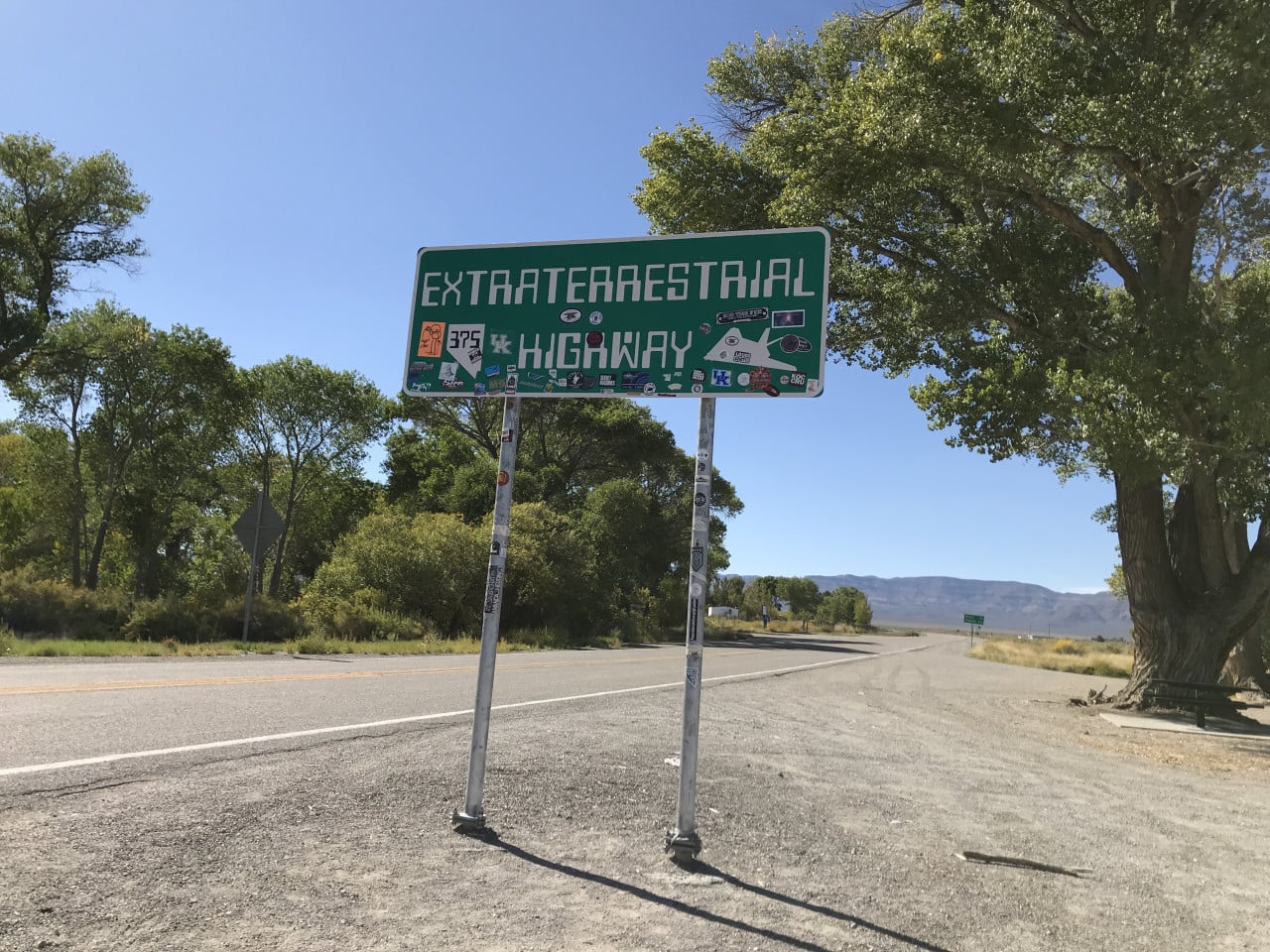 Značka Extraterrestrial Highway u nevadské silnice, obklopená stromy a pouští.