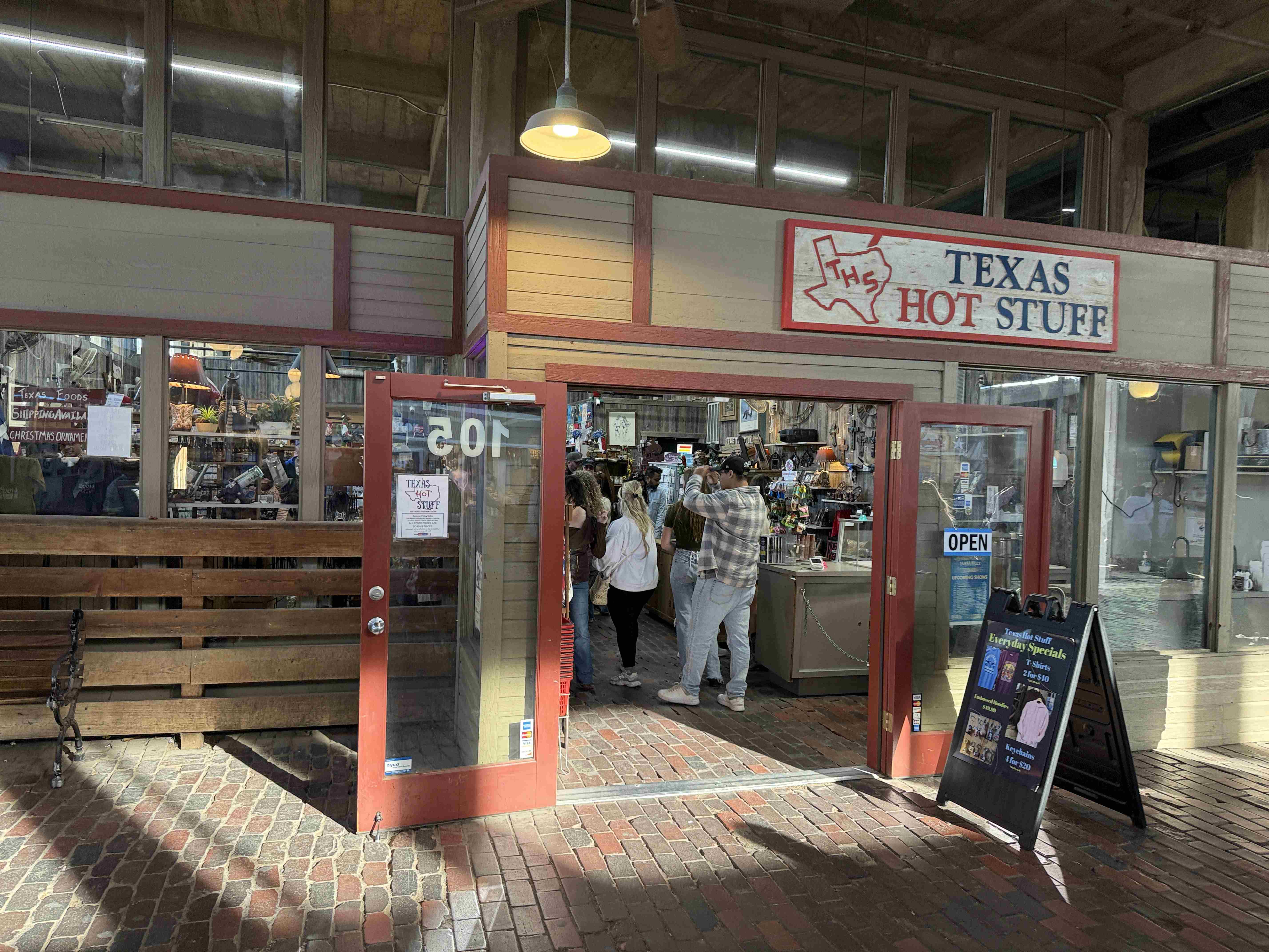 Vchod do obchodu TEXAS HOT STUFF, otevřené dveře, lidé uvnitř, OPEN.