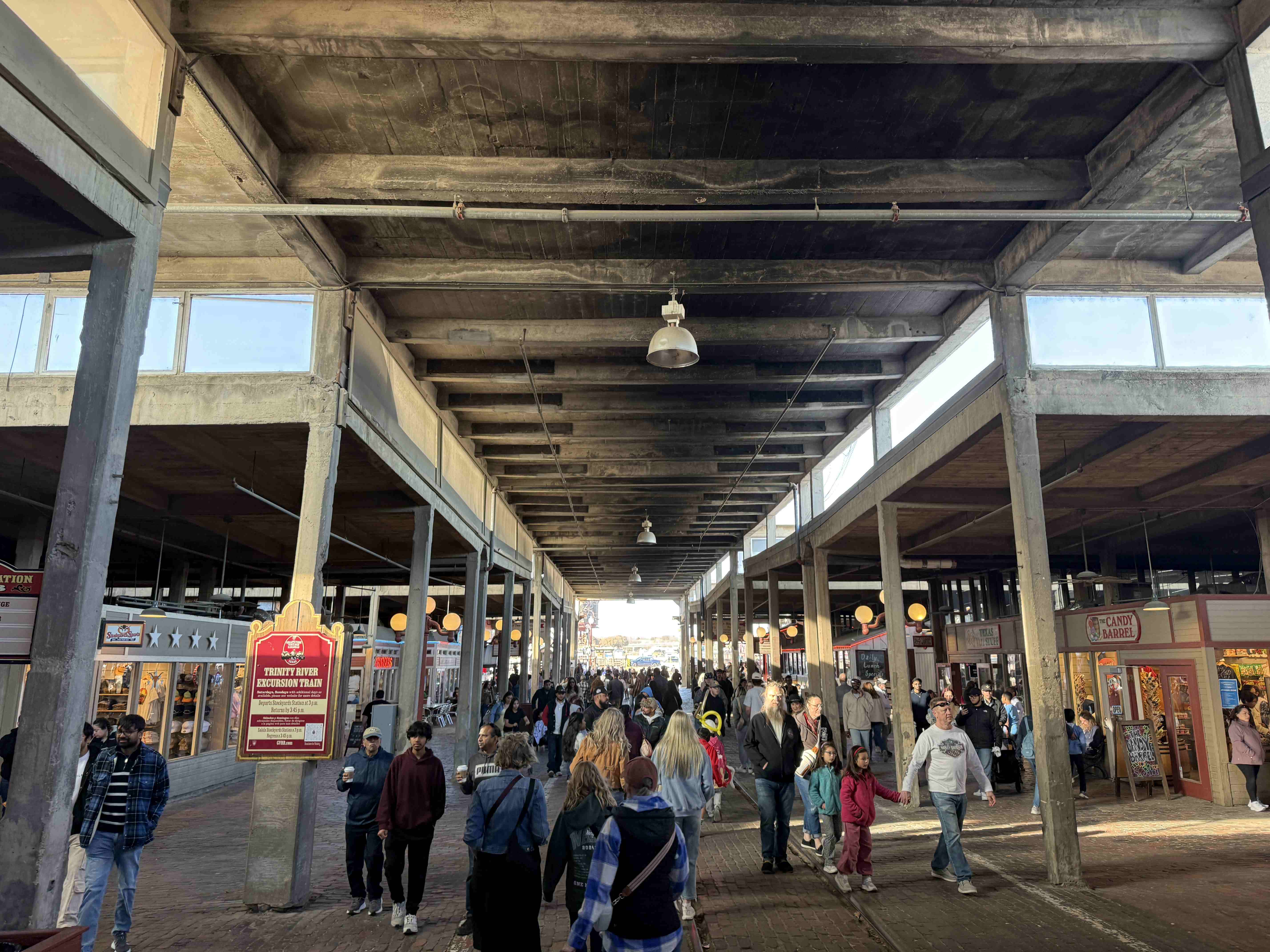 Dav ve Stockyards pod betonovou střechou, cedule TRINITY RIVER EXCURSION TRAIN, CANDY BARREL.