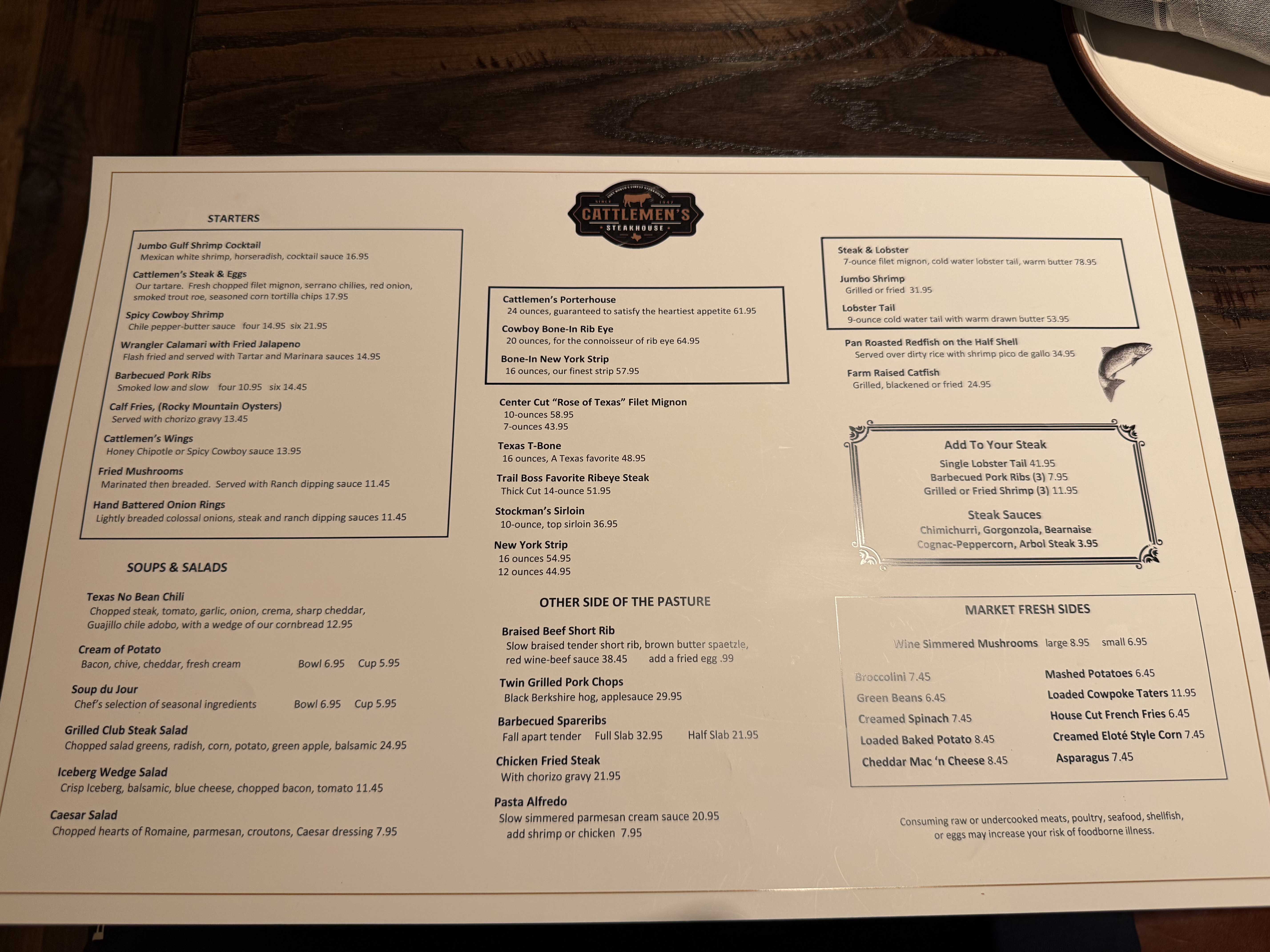 Jídelní lístek Cattlemen's Steakhouse na stole, nabídka steaků, mořských plodů a salátů.