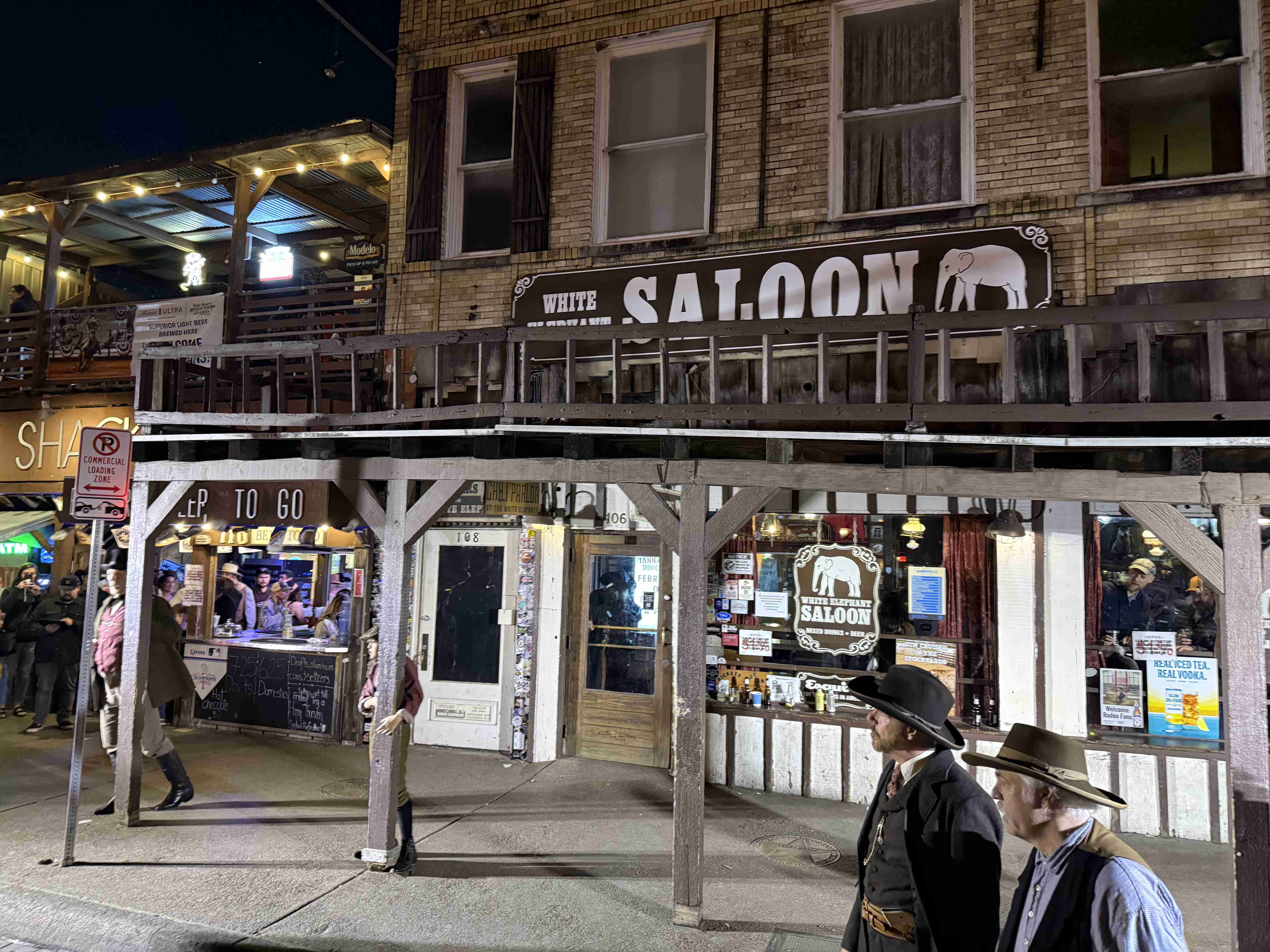 Noční ulice Stockyards, nápis WHITE SALOON, kovbojové v kloboucích na chodníku