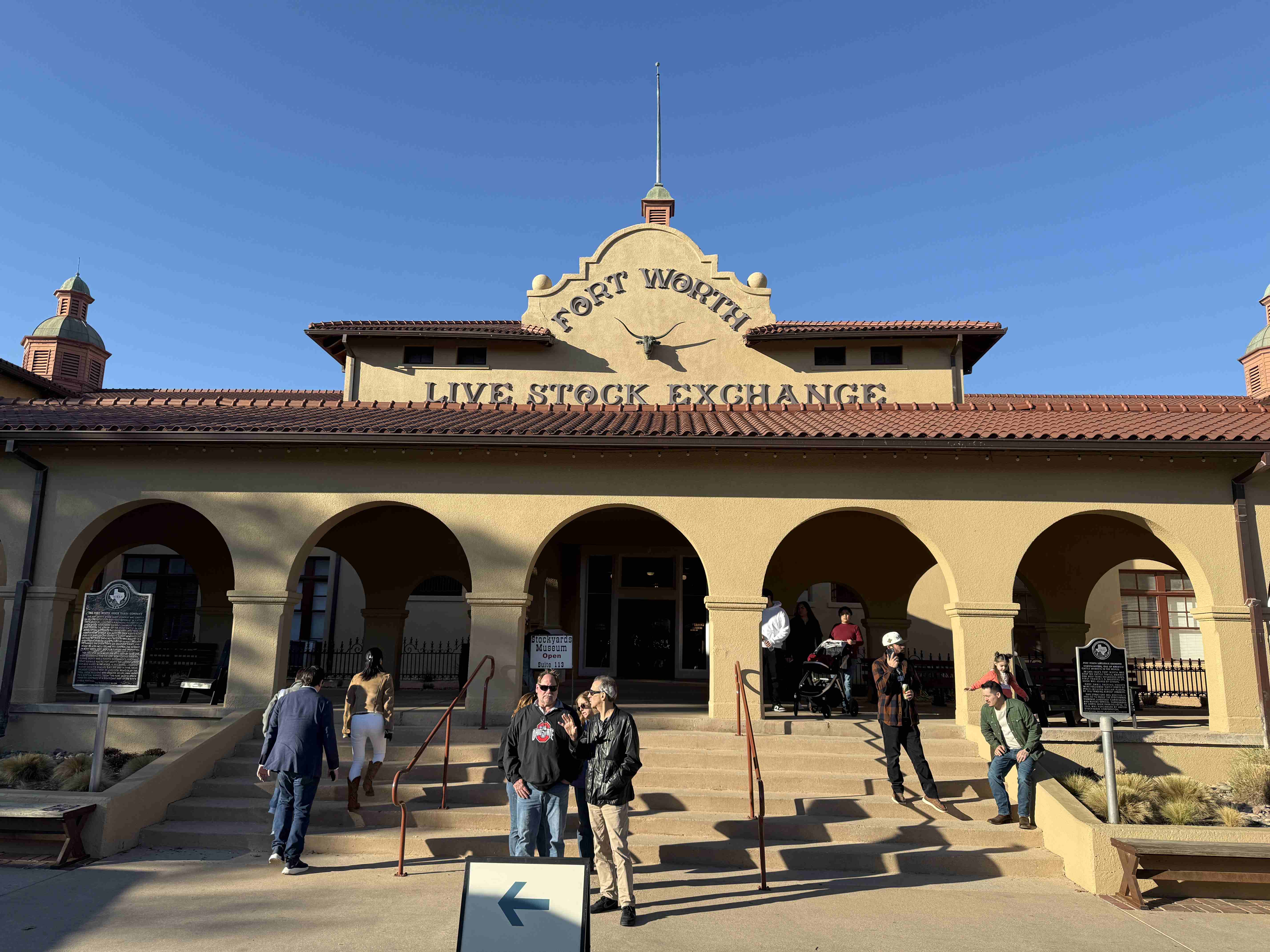 Fasáda budovy FORT WORTH LIVE STOCK EXCHANGE, oblouky a návštěvníci před vstupem.